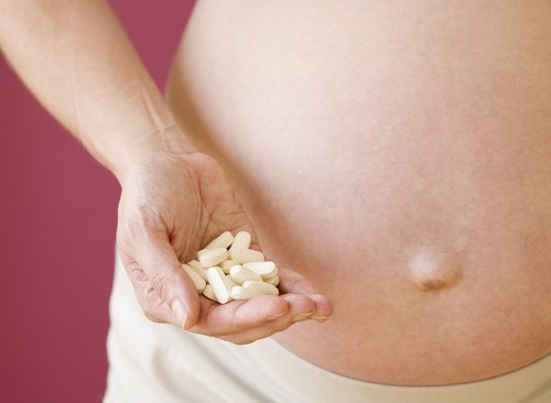Pregnant woman holding handful of vitamins