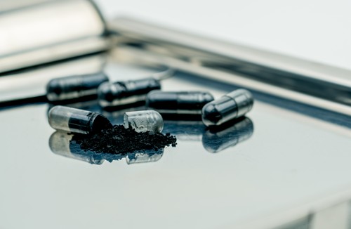 Activated charcoal capsule pills. Selective focus on black powder of activated charcoal on stainless steel drug tray. Medicinal carbon for relieves diarrhea, food or drug poisoning, flatulence.