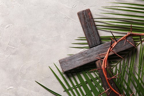Wooden cross with palm leaves and crown of thorns on grey background