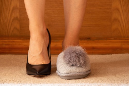 on one leg of high-heeled shoes and on the other leg the girl has slippers with a bubo on the floor of the house, different shoes on the girl's feet,
