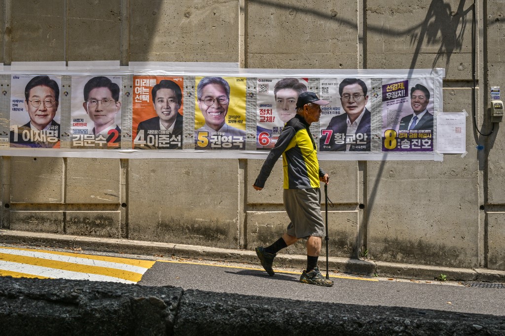 plakati predsjedničkih kandidata u južnoj koreji pored kojih na ulici prolazi muškarac