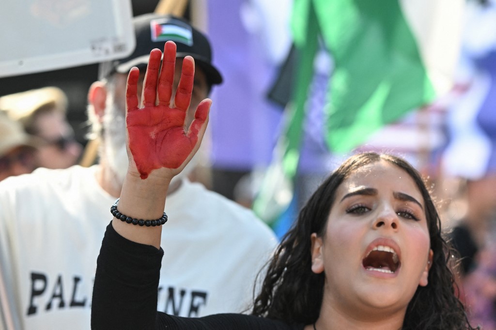 A woman has her hand painted red symbolizing blood as they take part in a "Solidarity with Palestine" demo in Berlin on August 9, 2025. (Photo by RALF HIRSCHBERGER / AFP)
