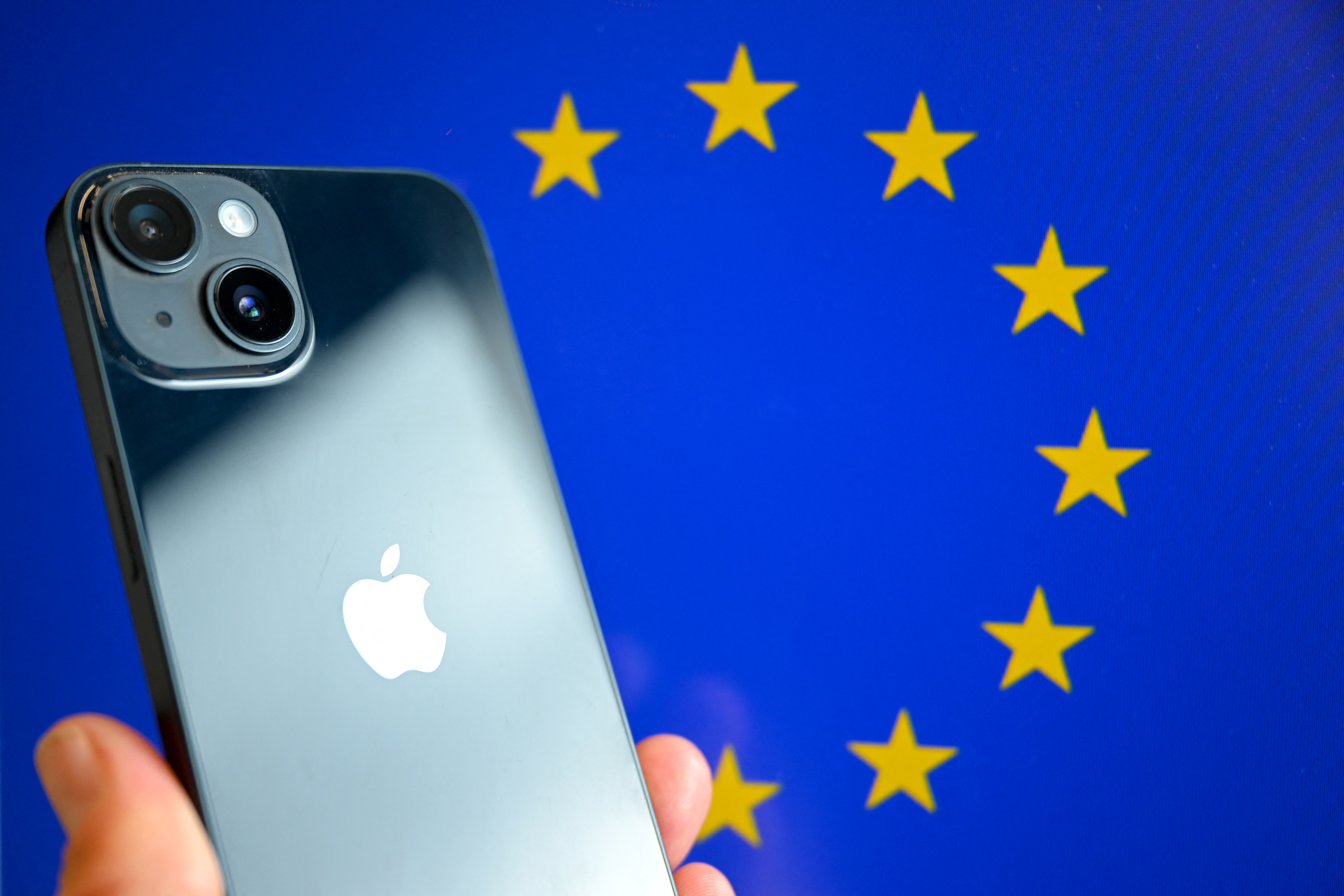 This photograph shows a hand-held smartphone with the Apple company logo and the European Union logo in the background, in Brussels on September 9, 2024. (Photo by Nicolas TUCAT / AFP)