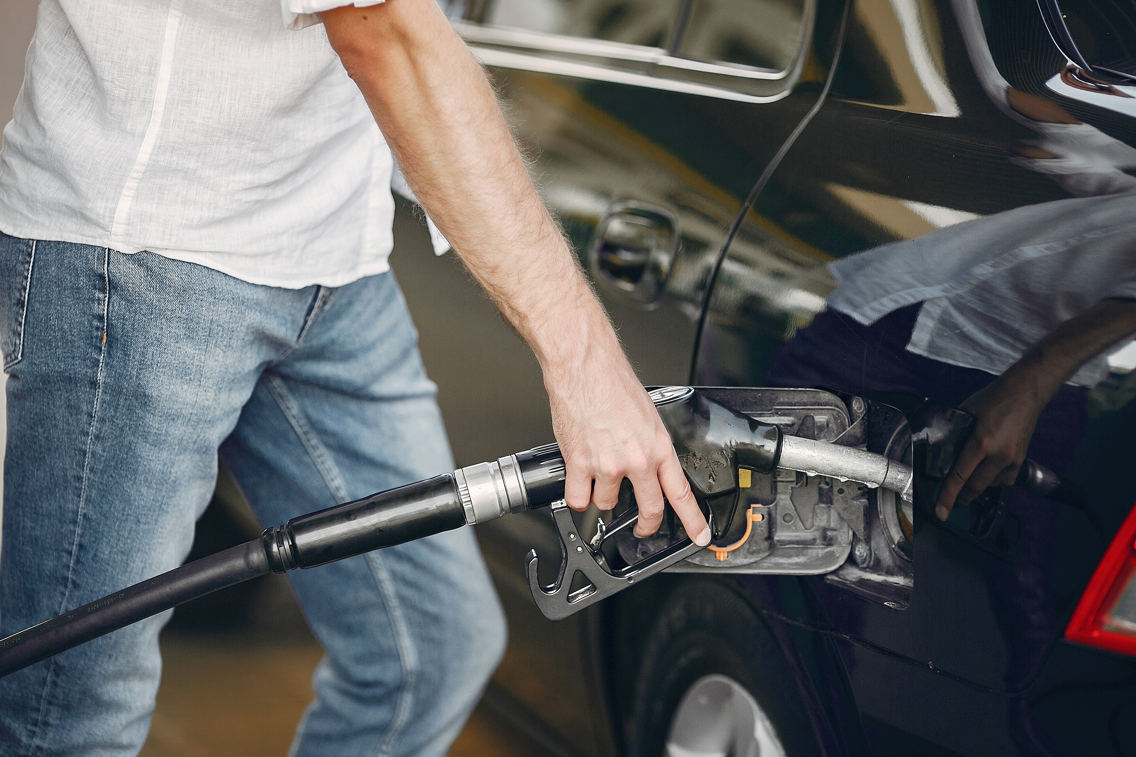 Man on a gas station. Guy refuelong a car. Male in a white shirt.
