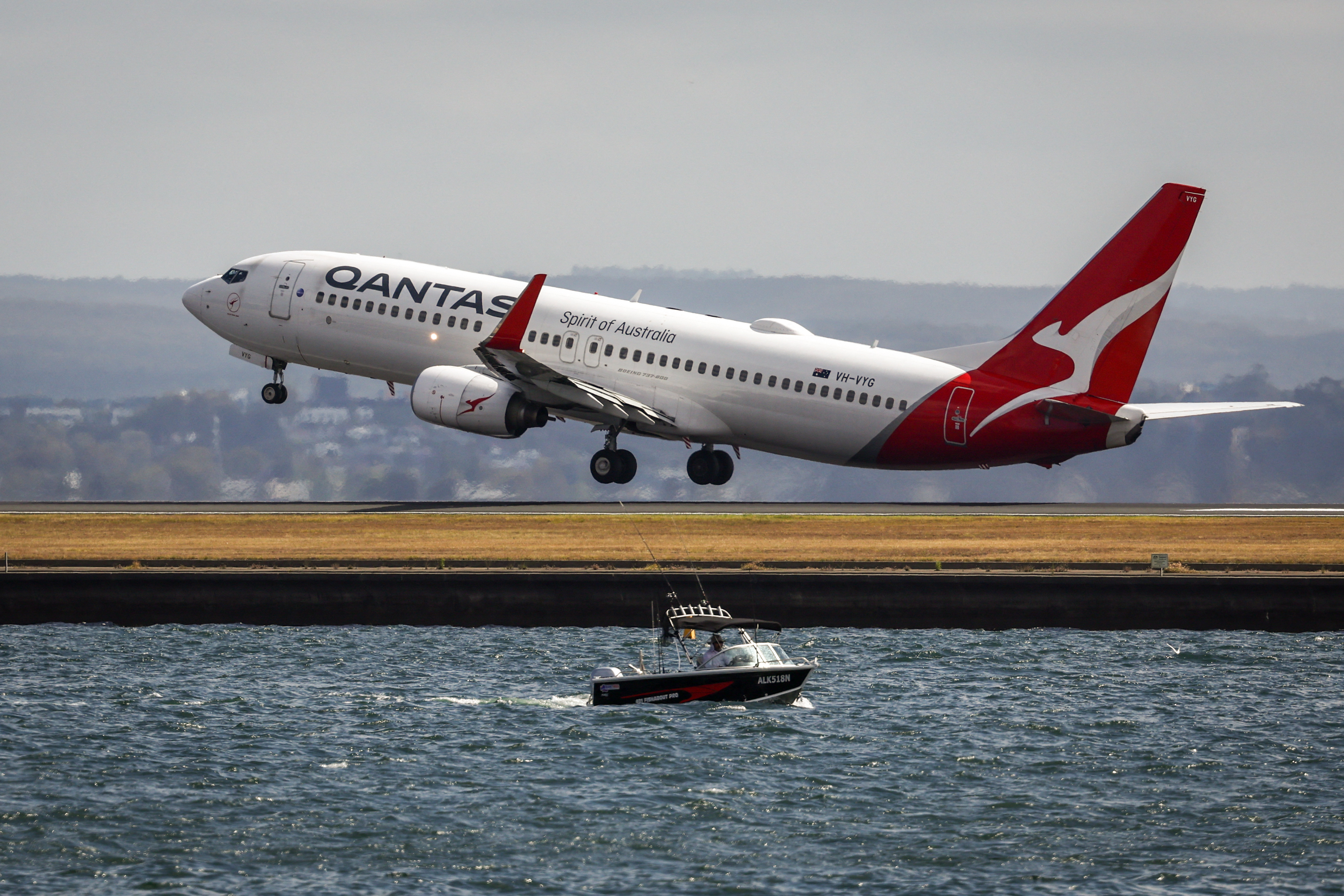 A fisherman drives his boat on Botany Bay as a Qantas Airways Boeing 737-838 airplane takes off at Sydney's Kingsford Smith international airport on November 3, 2023. (Photo by DAVID GRAY / AFP)