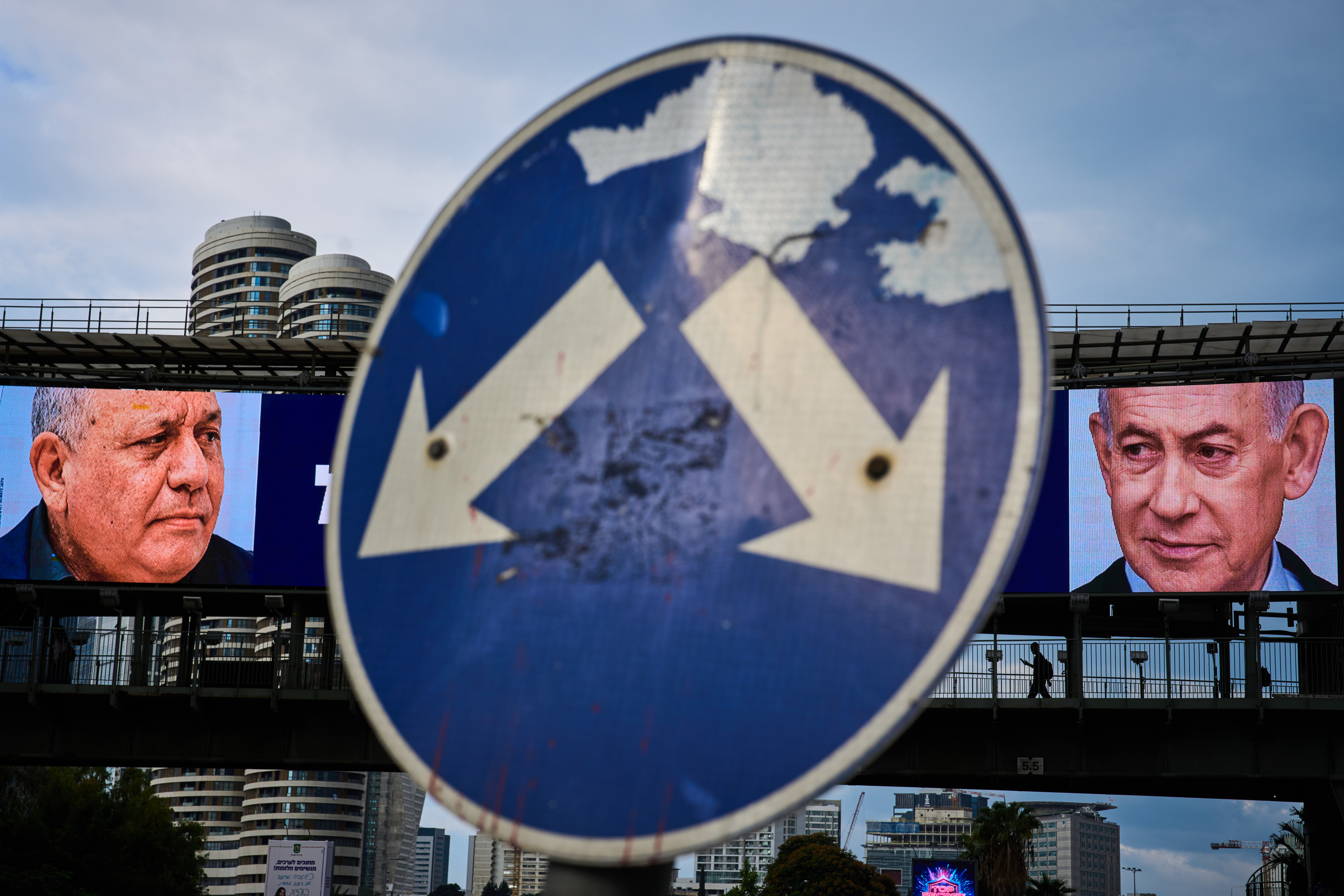 People cross a bridge beneath a television campaign advertisement featuring Israeli Prime Minister Benjamin Netanyahu, right, and his main rival, opposition candidate Gadi Eisenkot