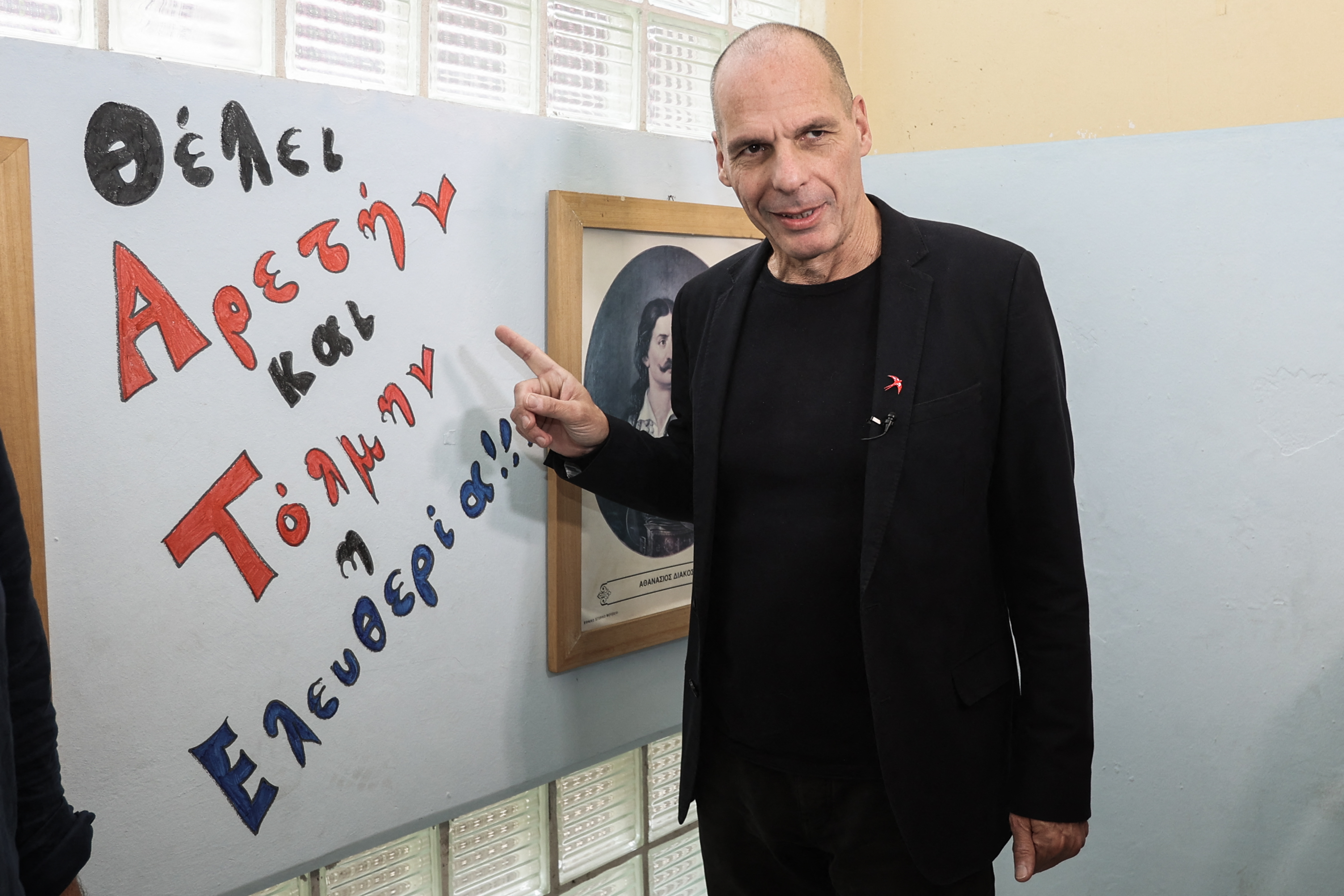 General Secretary of DiEM25 pan-European political movement Yanis Varoufakis, stands beside a slogan reading "Freedom needs virtue and courage" in a polling station in Perama, on May 21, 2023