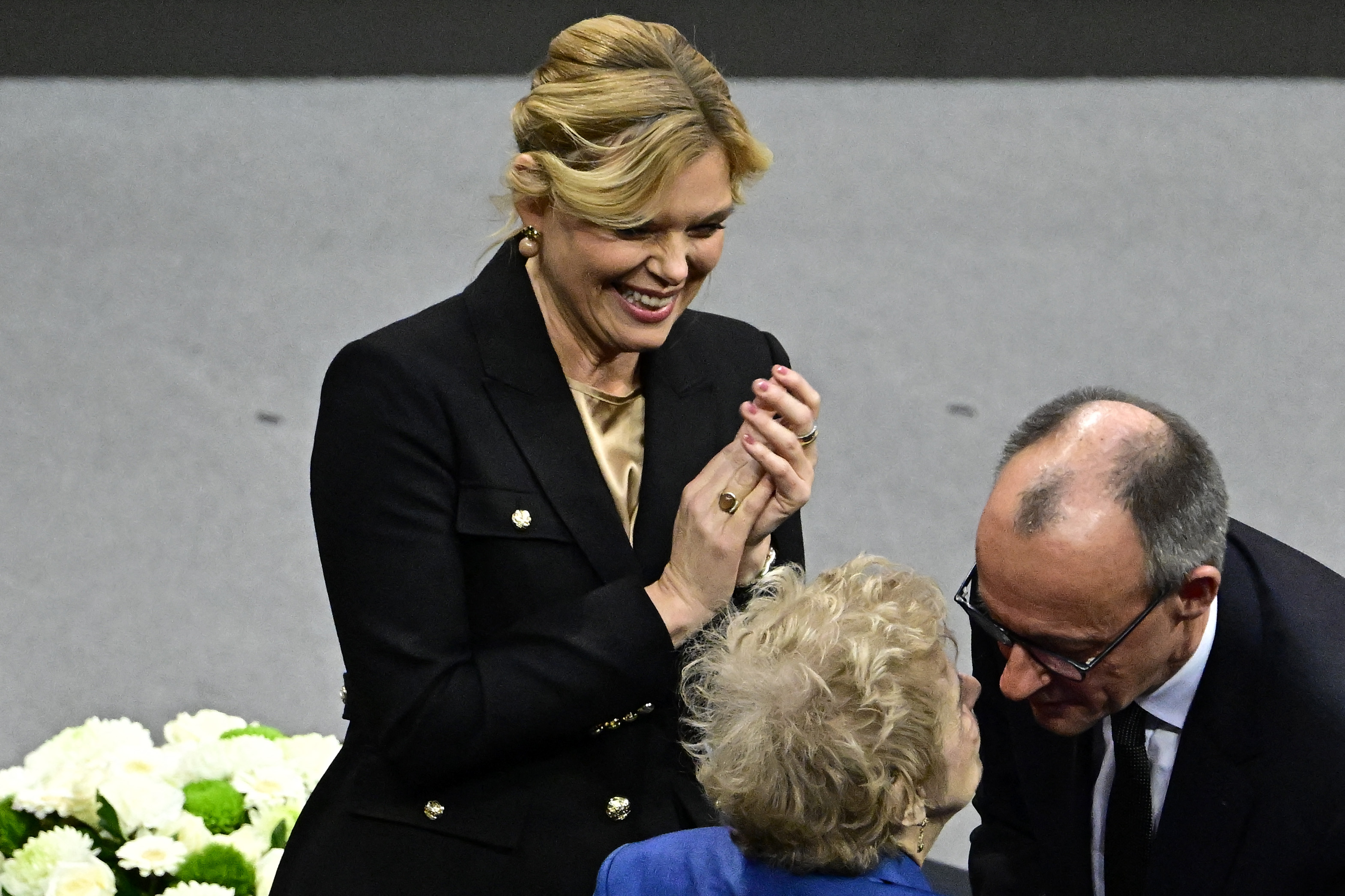 Holocaust survivor Tova Friedman (C) is hugged by German Chancellor Friedrich Merz (R) and applauded by the President of the Bundestag