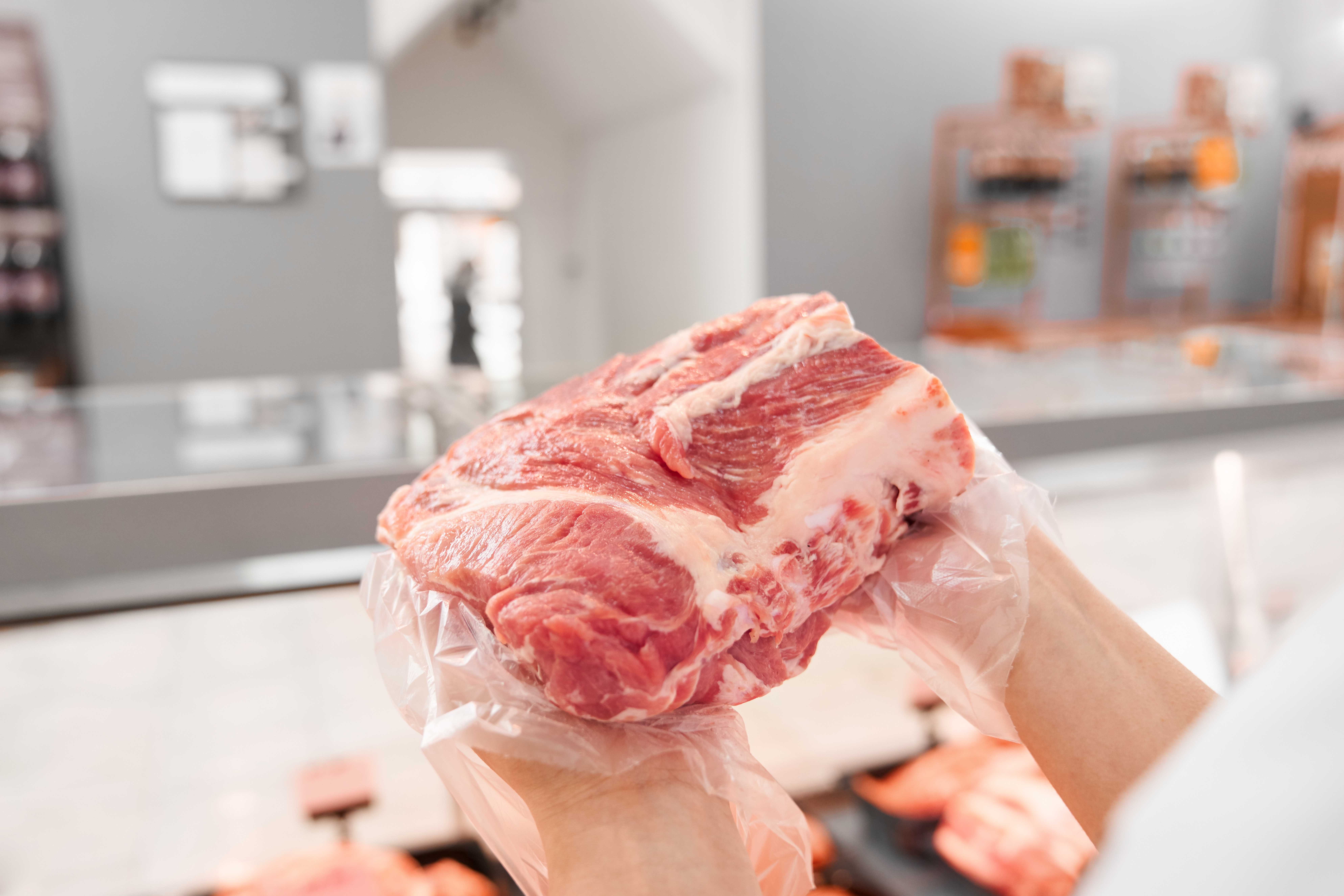 Selective focus of fresh red raw piece of meat in hands of young incognito woman. From above view of girl standing behind counter with big variety of meat and showing pork from refrigerator.