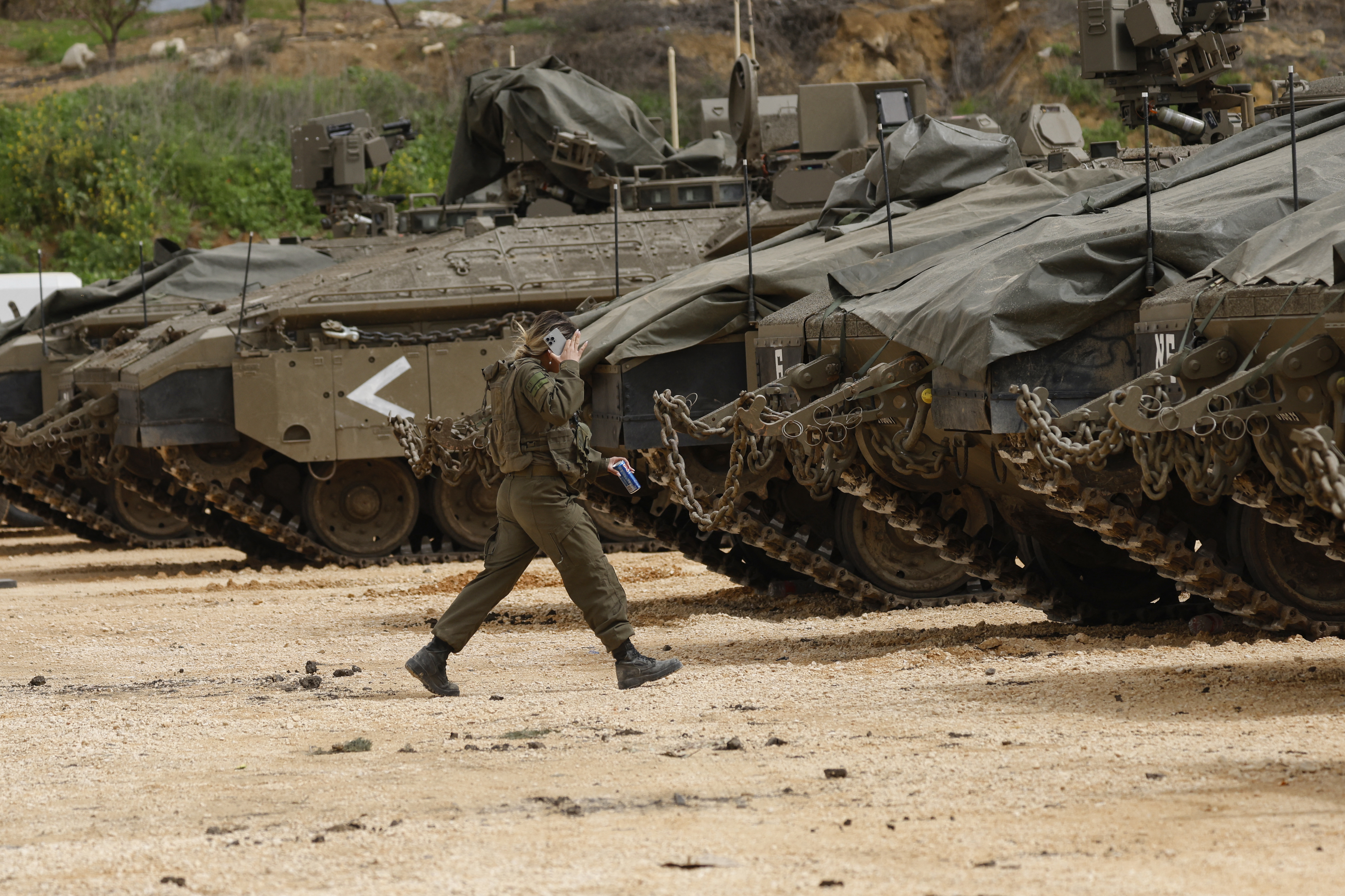 A female Israeli soldier walks towards army tanks gathered in the upper Galilee near the Israel-Lebanon border on March 14, 2026.