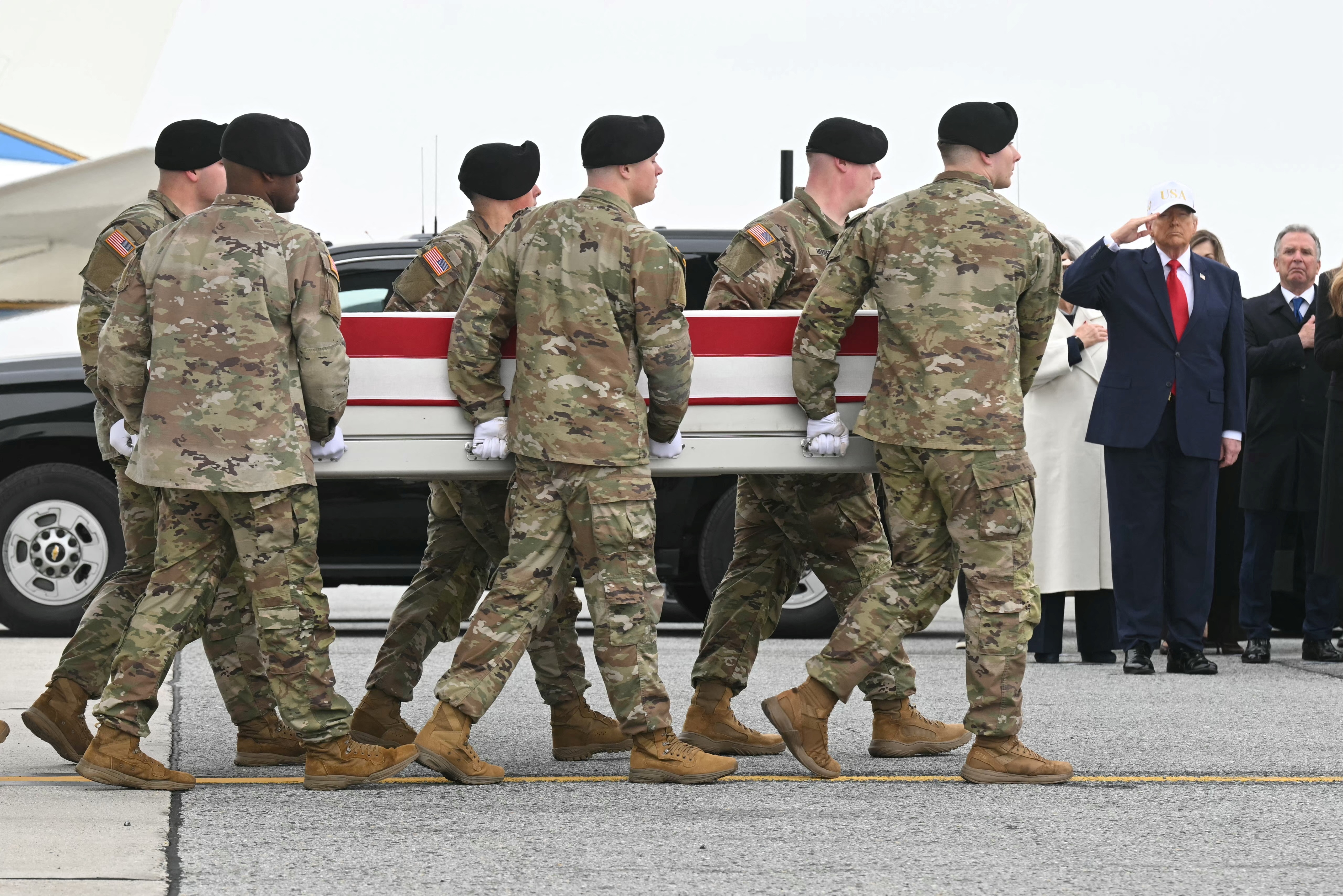 US President Donald Trump salutes as members of a US Army team carry the flagged-drapped transfer case