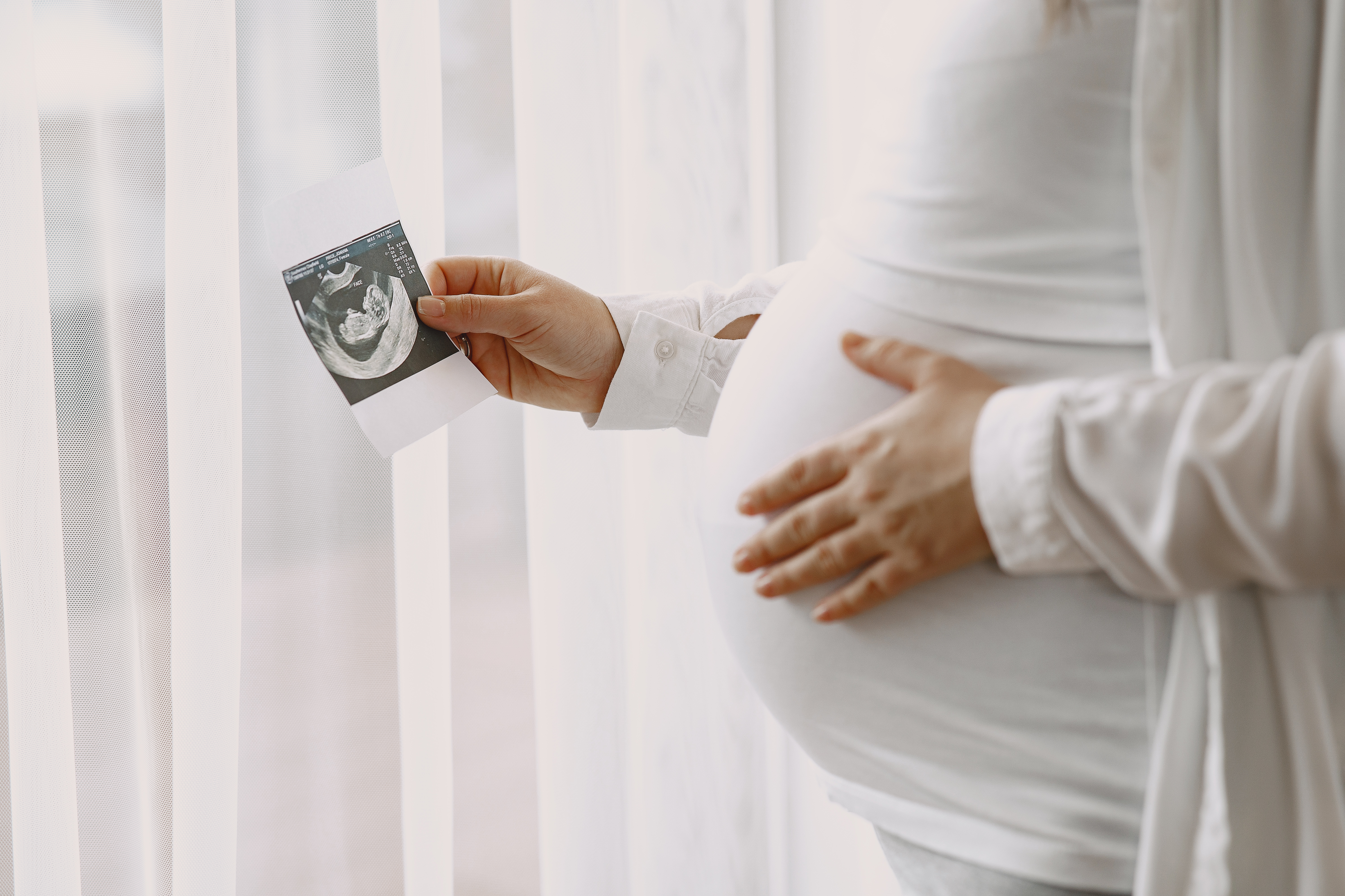 Woman standing by the window. Pregnant looking at photo. Woman expecting a baby.