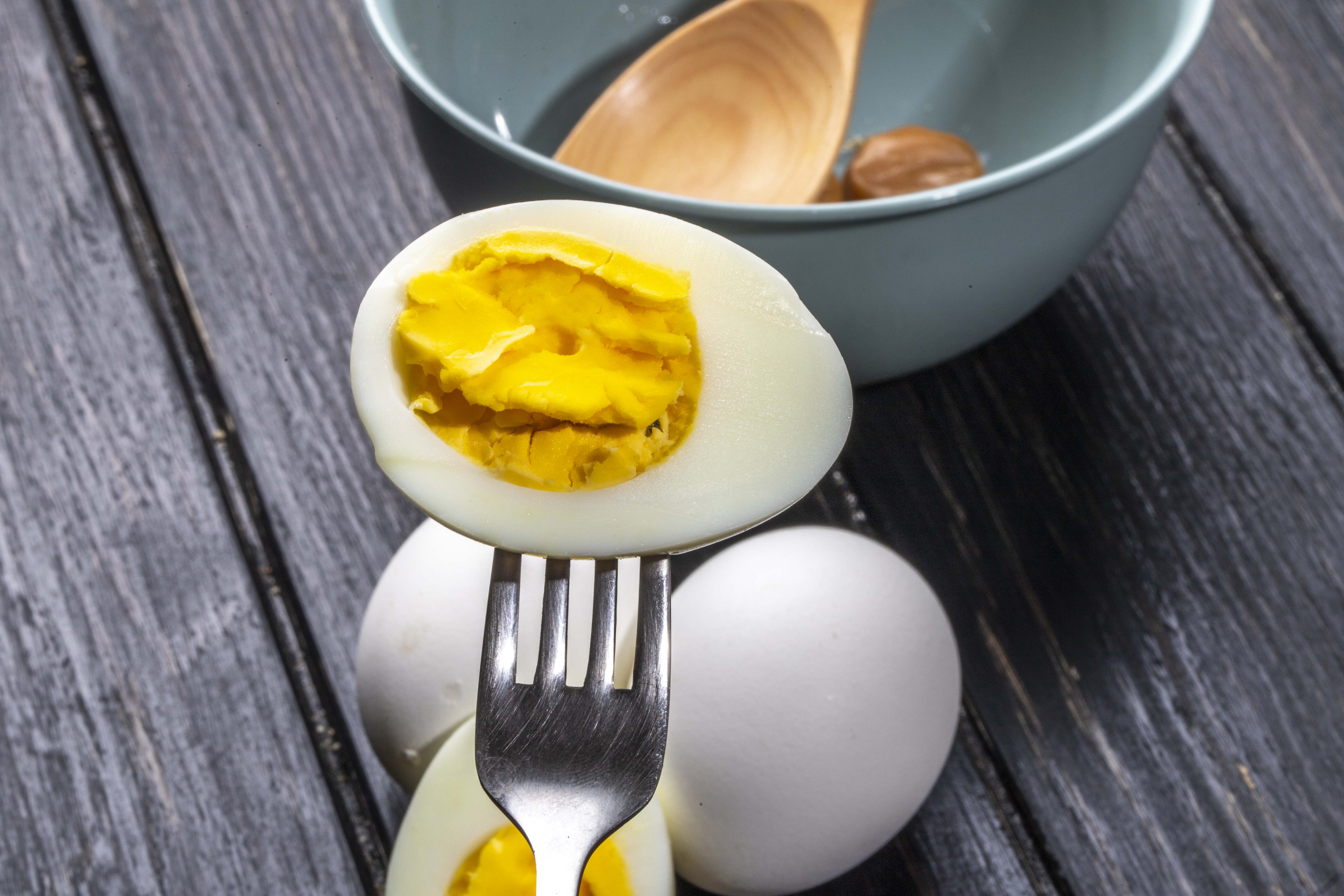 side view of boiled egg half with fork on wooden rustic background