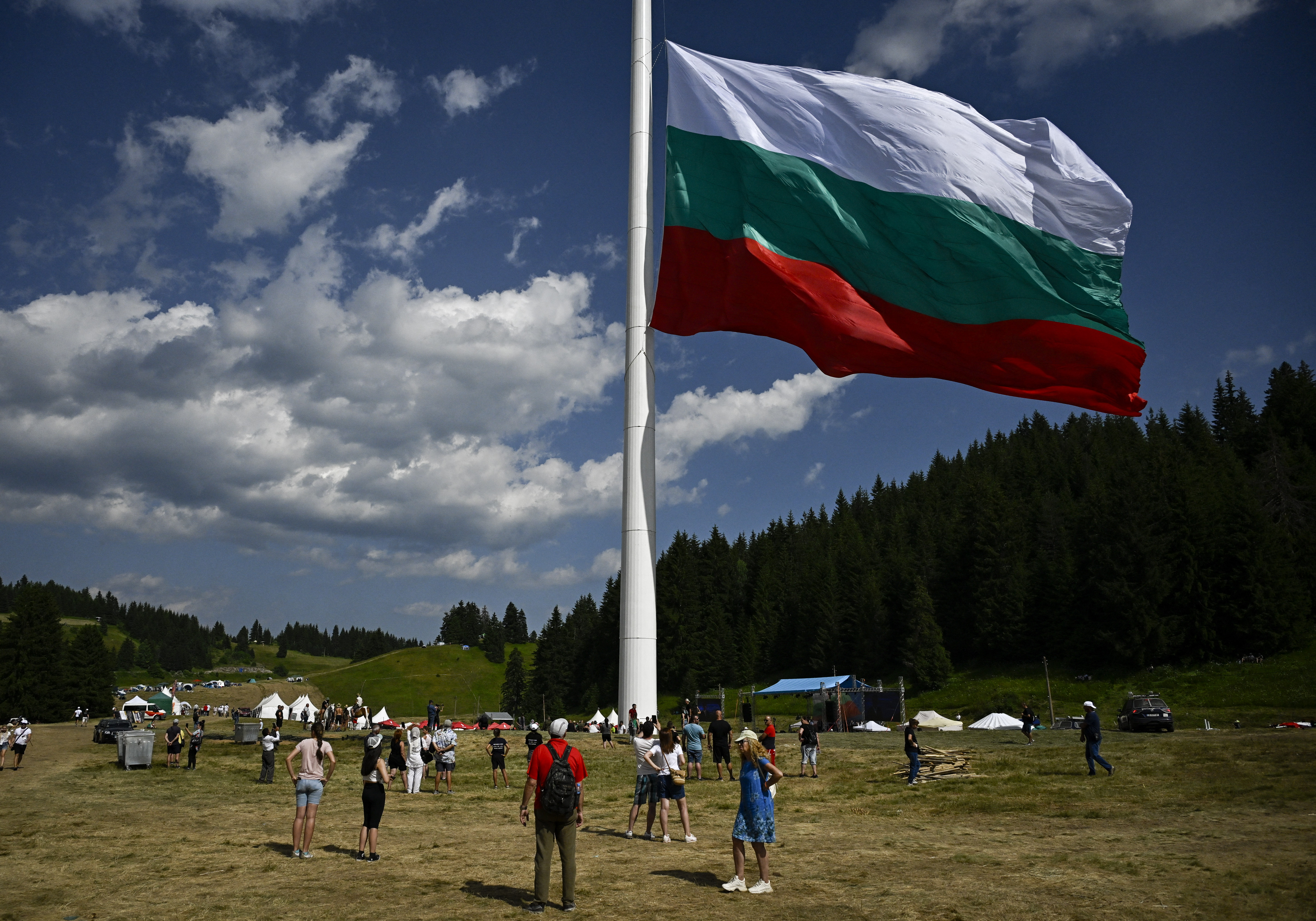 People watch the rising of a large Bulgarian flag during preparations ahead of the inauguration of an 111 m / 364 ft flagpole at Rozhen meadows near the city of Smolyan, some 80km south of Plovdiv, on July 13, 2023.