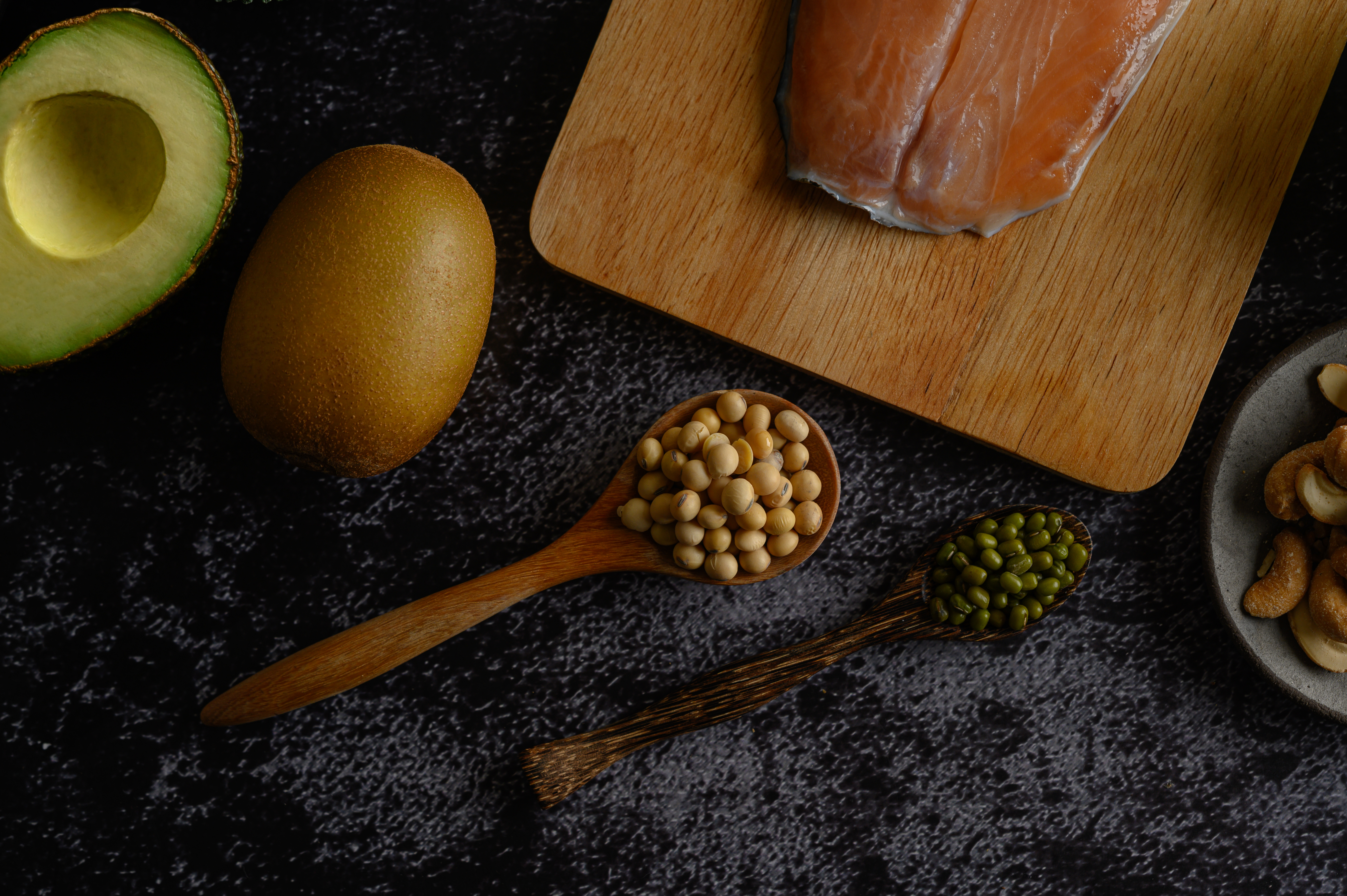 legumes, salmon pieces and kiwi on a black cement floor background.