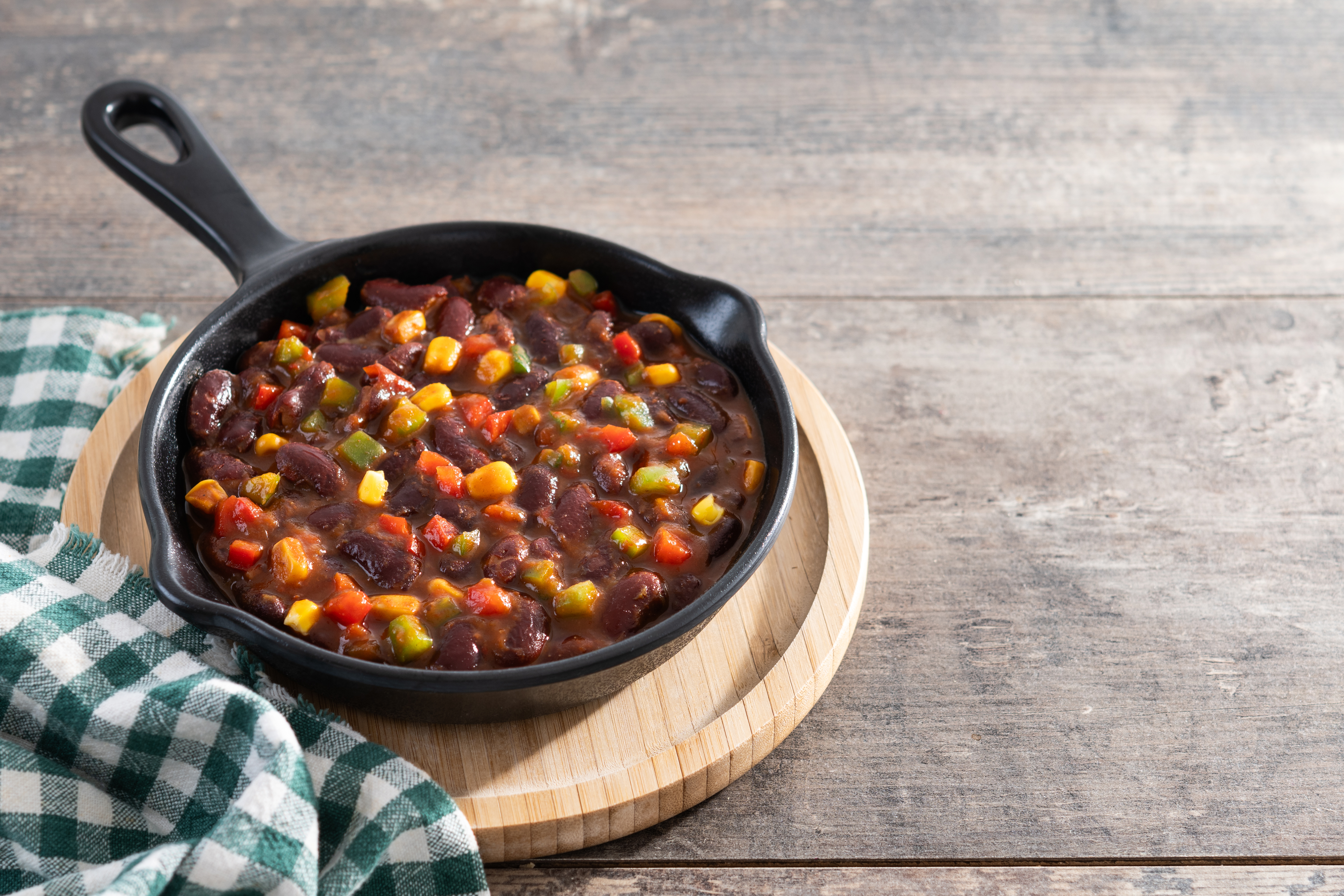 Mexican chilli beans with vegetables in iron pan on wooden table