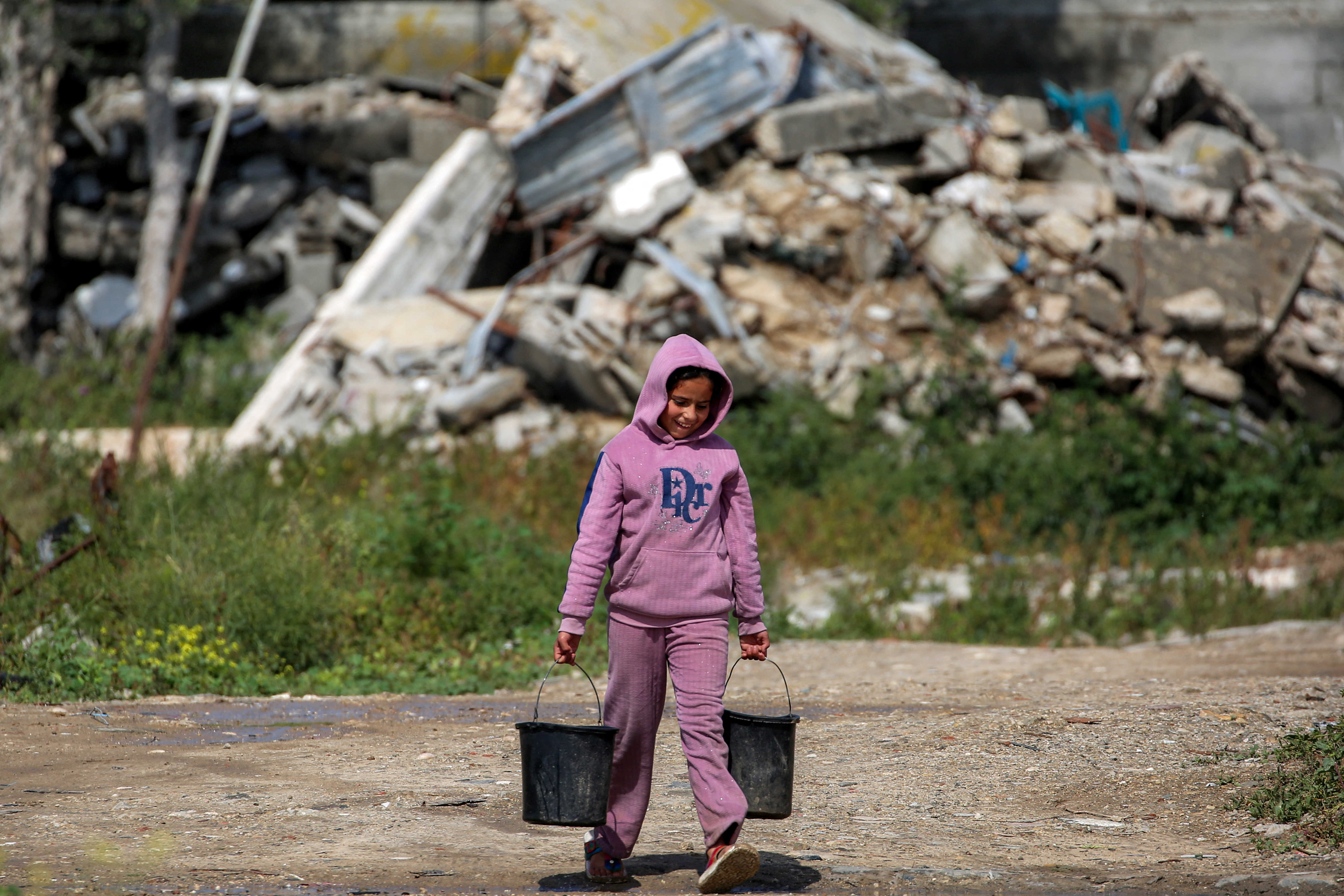 A girl walks with pails of water filled from a nearby cistern at the Bureij camp for Palestinian refugees in the central Gaza Strip on March 27, 2026.