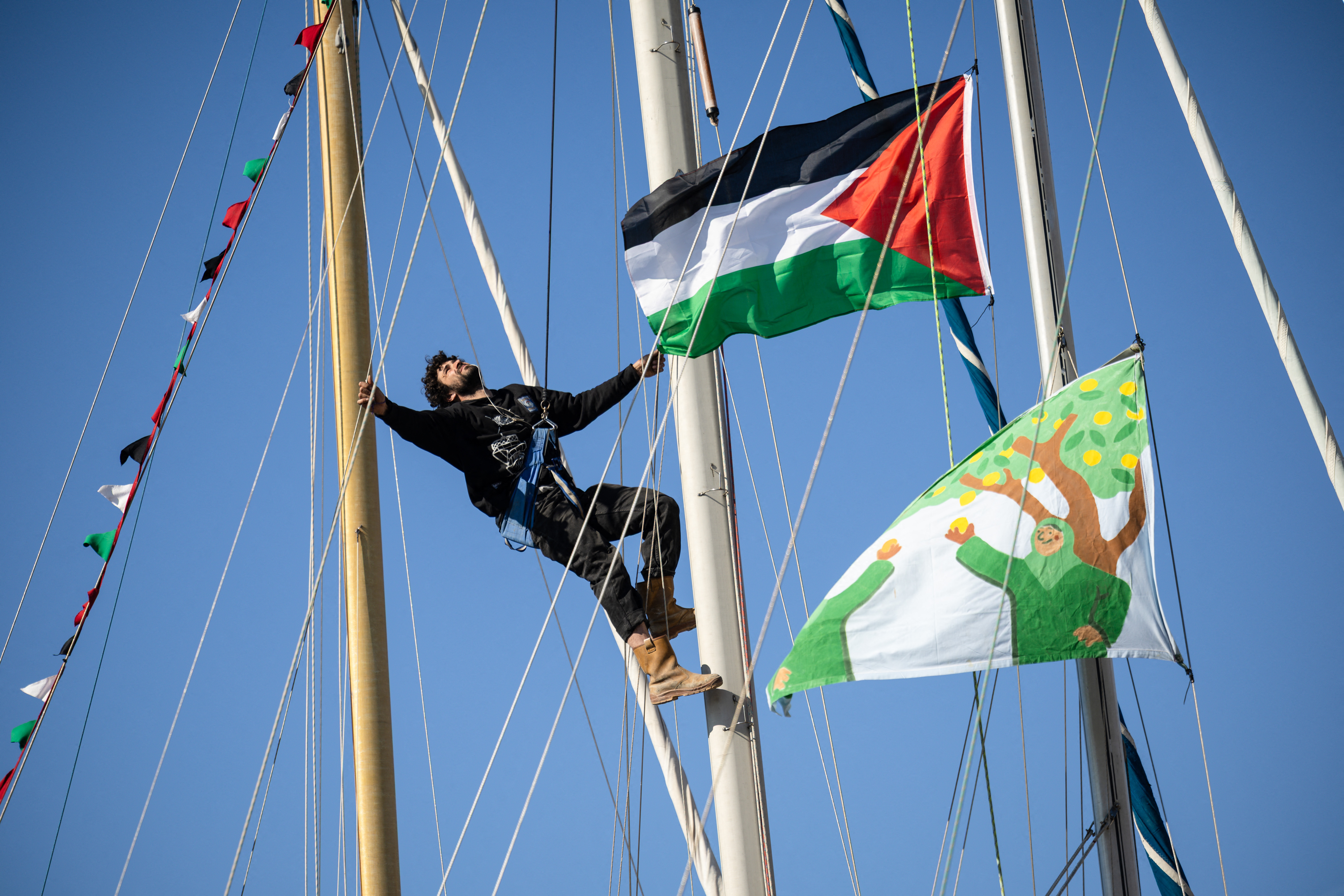 An activist climbs the mast of a boat displaying a Palestinian flag in l'Estaque, part of Marseille's harbour, southern France, on April 4, 2026, during a rally in support of a flotilla carrying activists from “Thousand Madleens to Gaza”