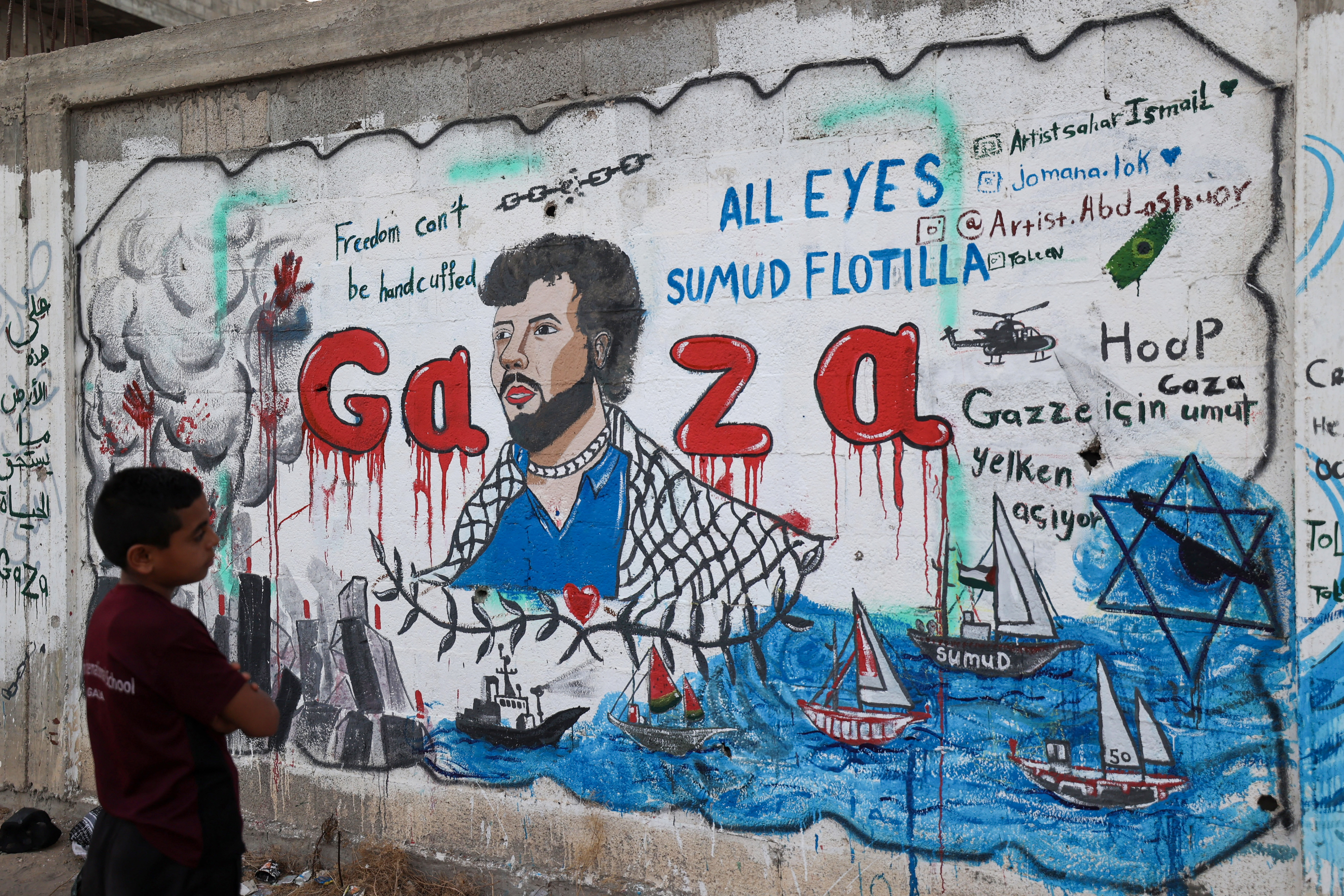 A Palestinian boy looks at a mural depicting Israel's interception of ships participating in the Global Sumud Flotilla, a civilian-led humanitarian aid mission to Gaza by sea, in Nuseirat in the central Gaza Strip