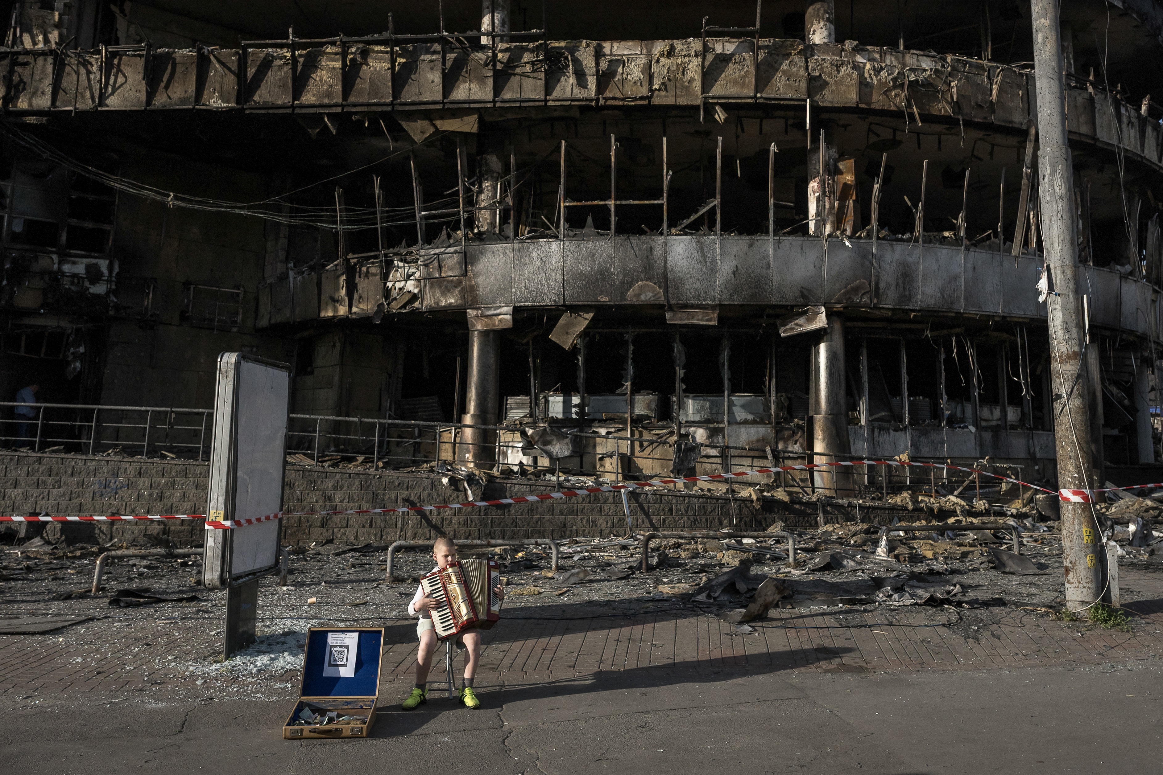 A boy plays the accordion in front of a shopping center damaged by Russian strikes in Kyiv on May 25, 2026, amid the Russian invasion of Ukraine. (Photo by Vladyslav Musiienko / AFP)