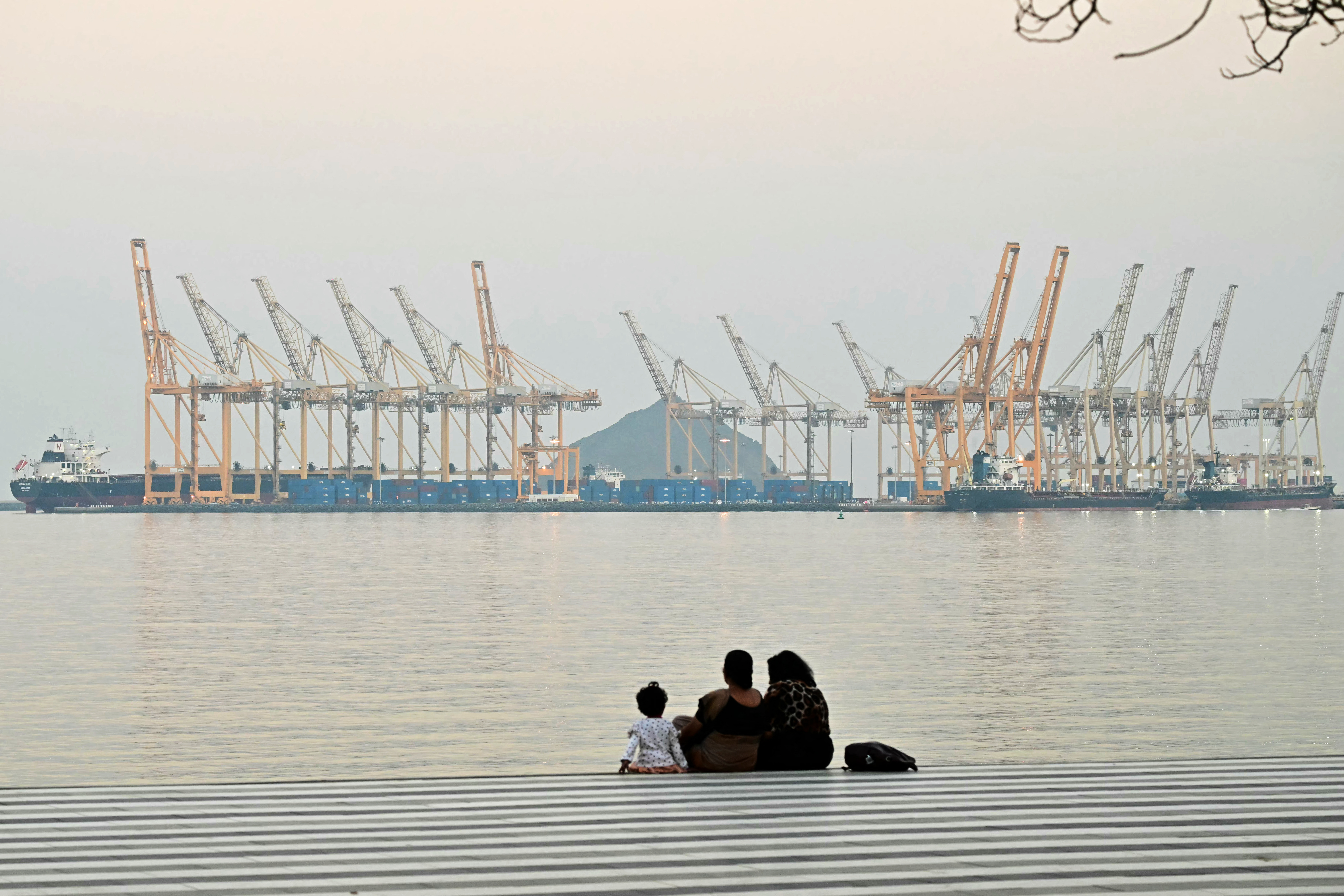 A family sits against the backdrop of a dockyard in Khor Fakkan in the Gulf emirate of Sharjah, off the coast of the Gulf of Oman, on February 25, 2026. (Photo by Giuseppe CACACE / AFP)