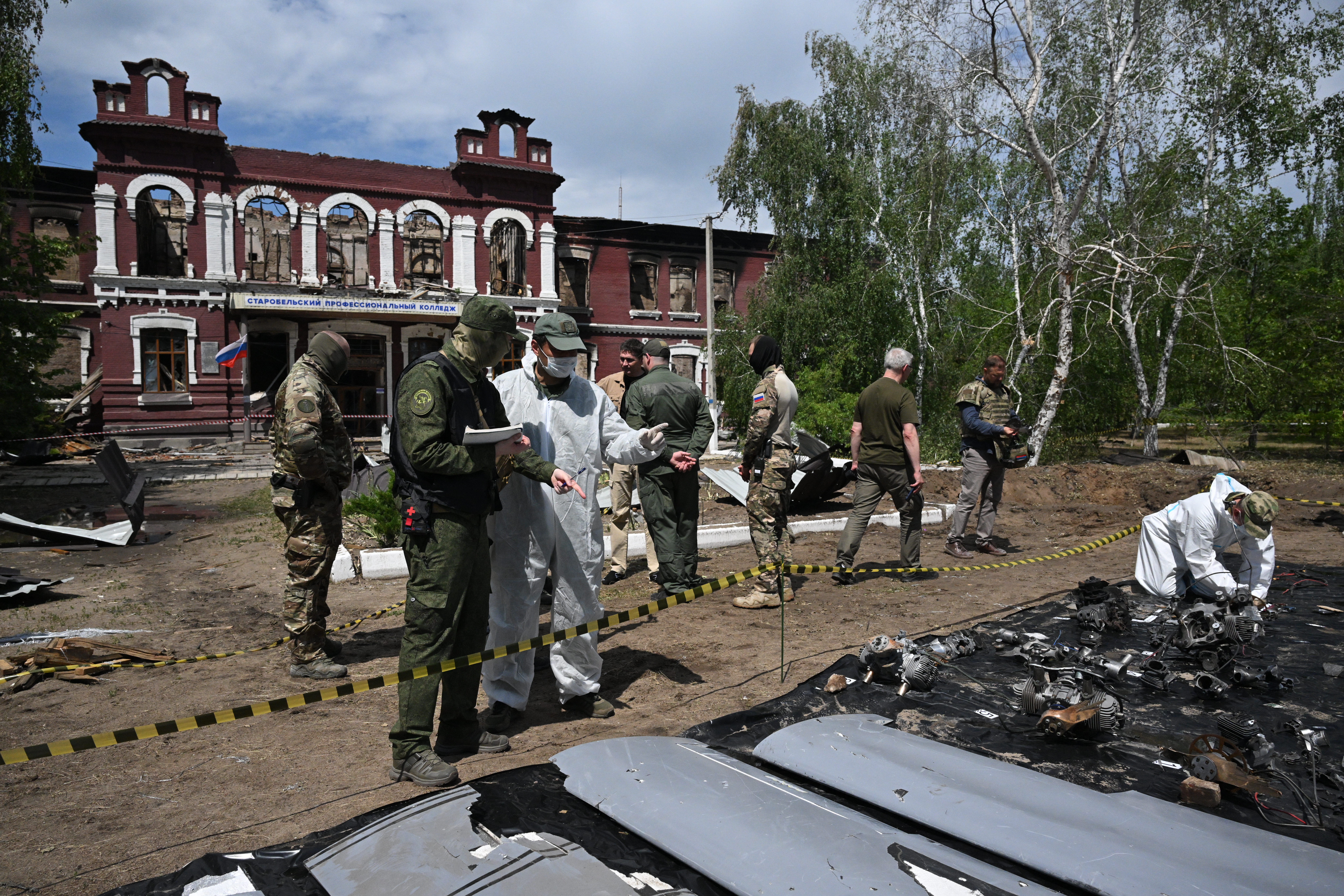 A Russian investigator examines what is presented by Russian authorities as parts of Ukrainian drones outside the destroyed building of the Starobilsk professional college of the Luhansk Pedagogical University