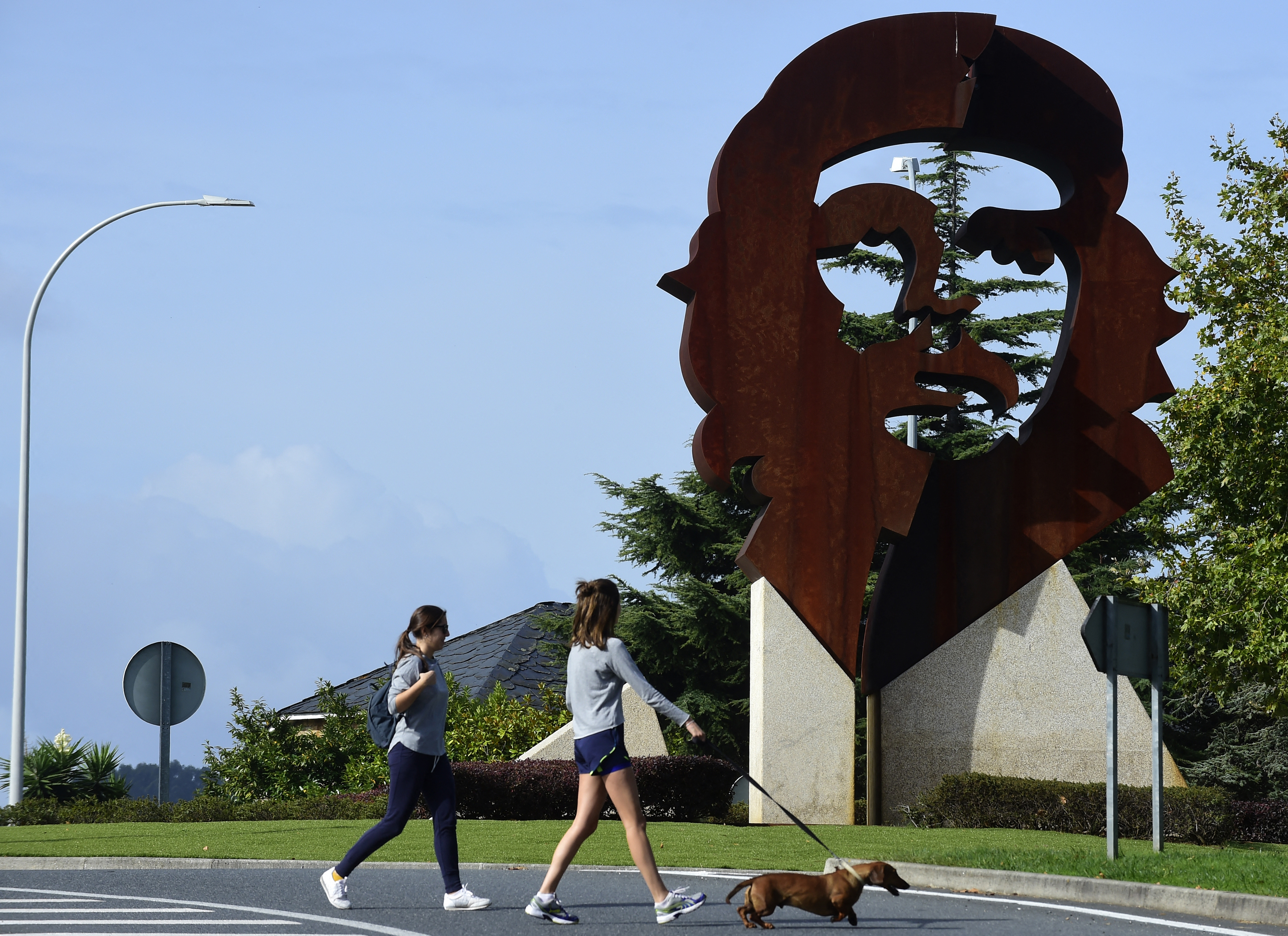 Two girls walk a dog past a monument dipicting the image of late Argentinian revolutionary legend Ernesto "Che" Guevara, in Oleiros, some 10 km from Coruna, northwestern Spain