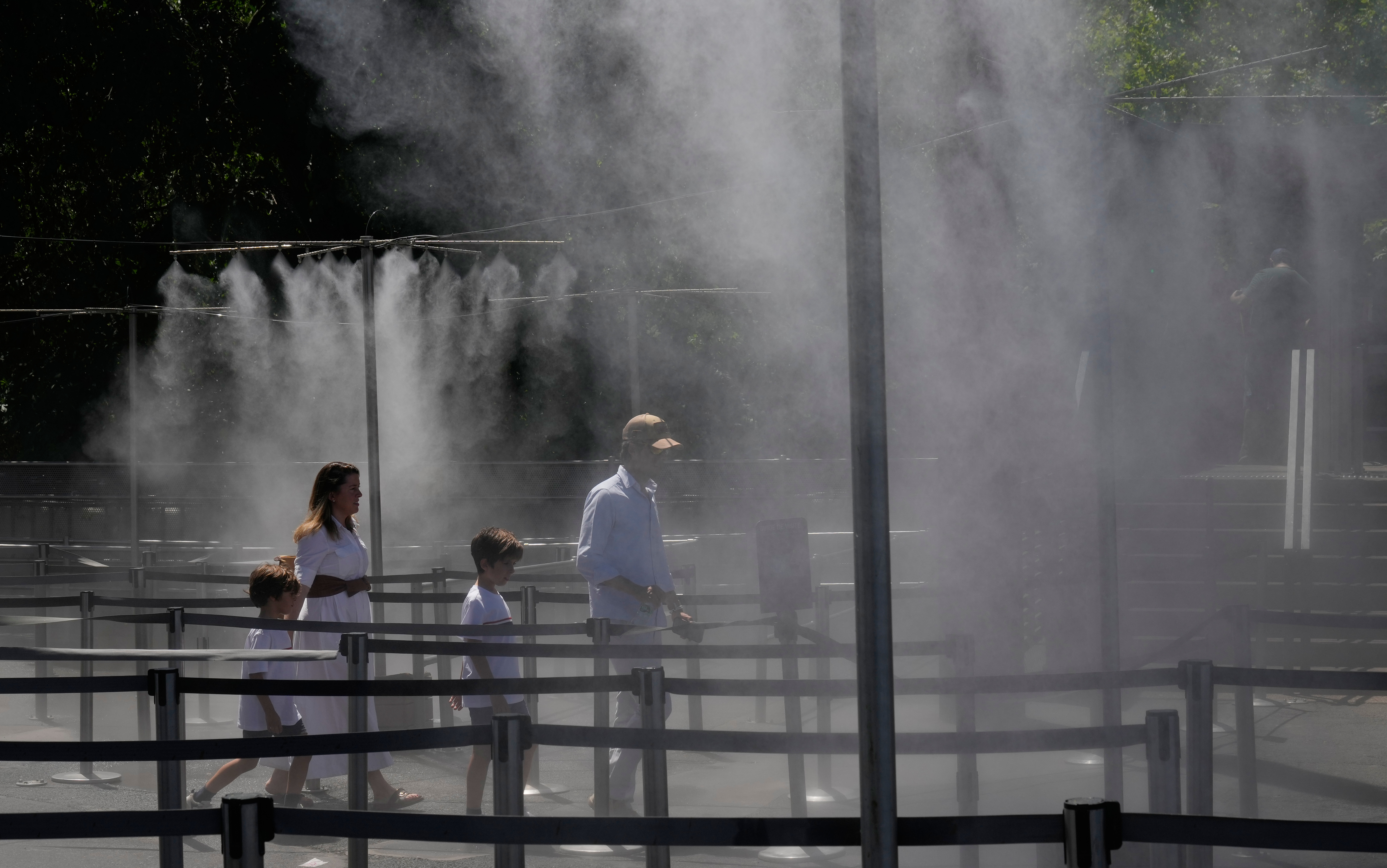 A family walks through a cooling water spray at the Eiffel Tower in Paris, Sunday, June 21, 2026. (AP Photo/Michel Euler)