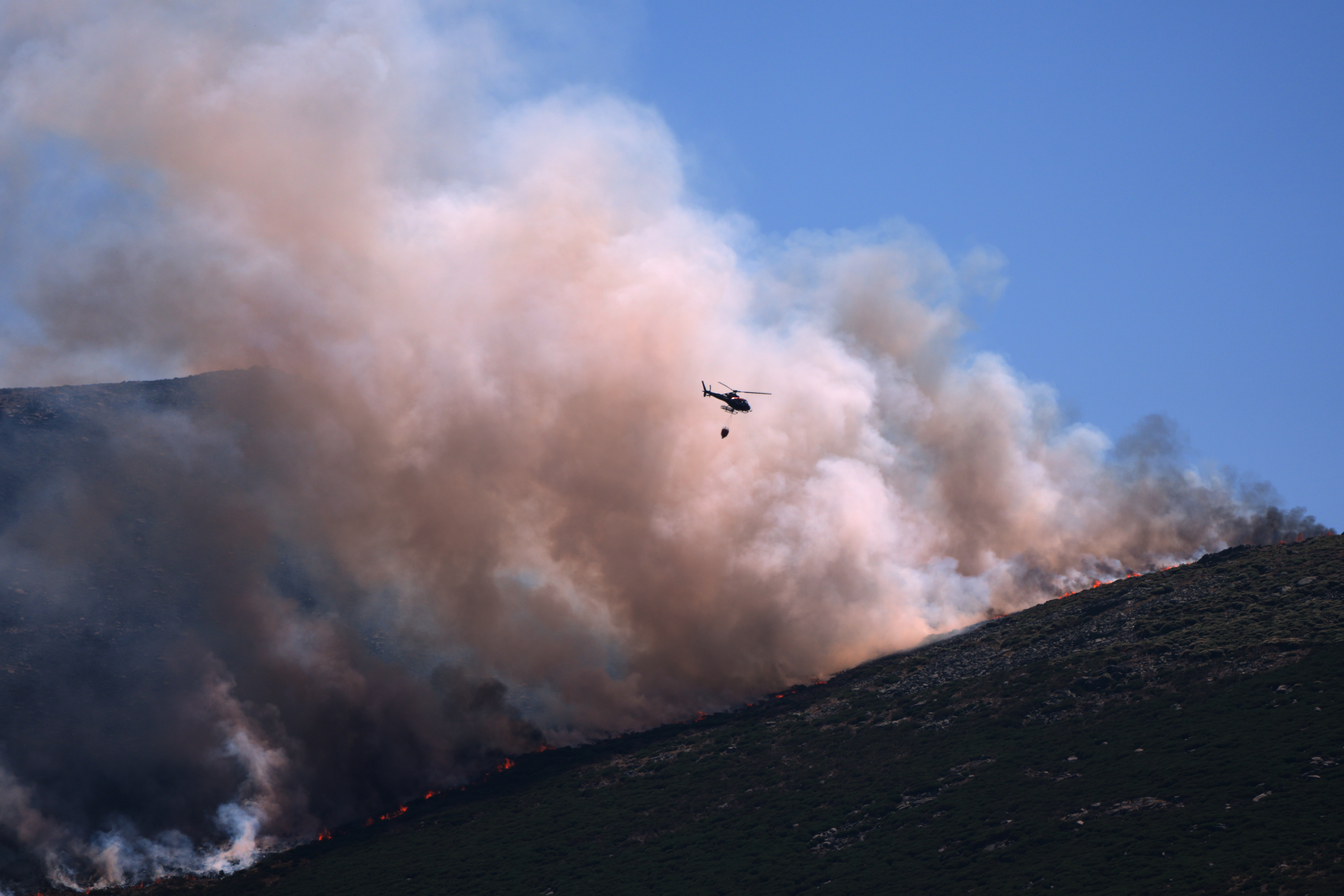 A firefighting helicopter drops water on the flames. (AP Photo/Manu Fernandez)