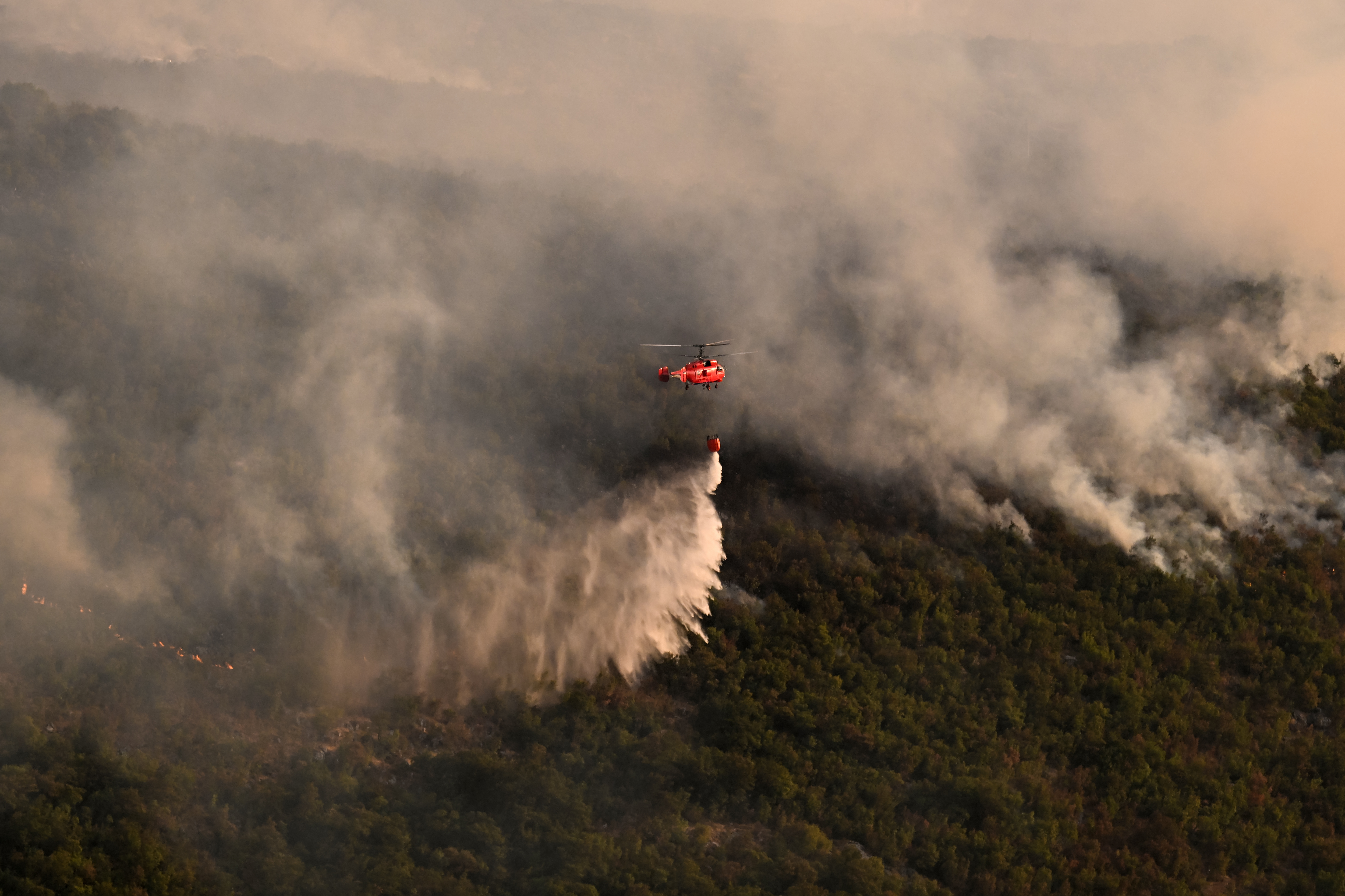 A Serbian Kamov Ka-32 firefighting helicopter drops water over a wildfire raging in the outskirts of the Podgorica capital, on August 12, 2025