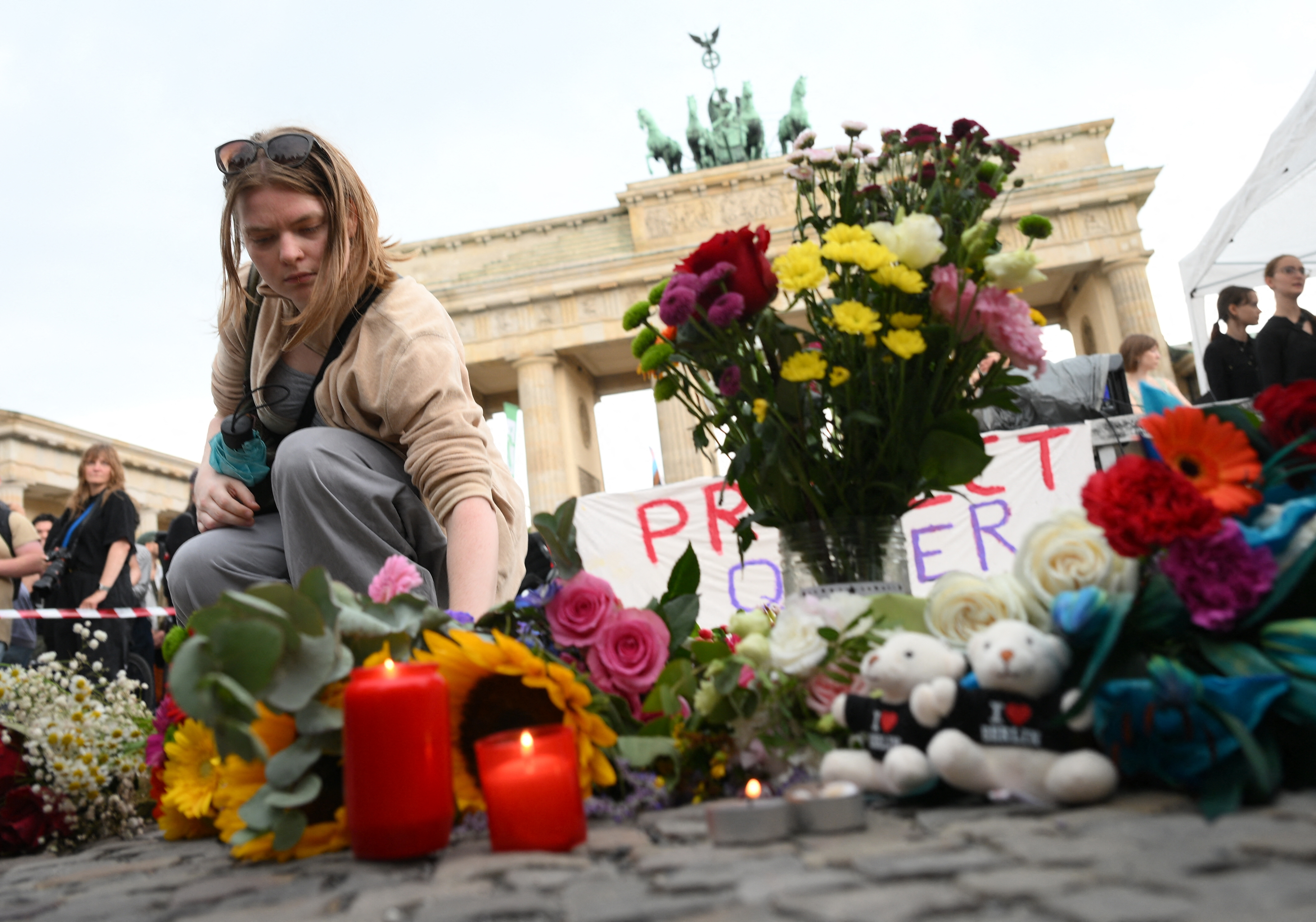 A mourner places flowers on July 26, 2026 in front of landmark Brandenburg Gate during to a so-called "community mourning" one day after the car ramming attack on people on the outskirts of Berlin's Christopher Street Day