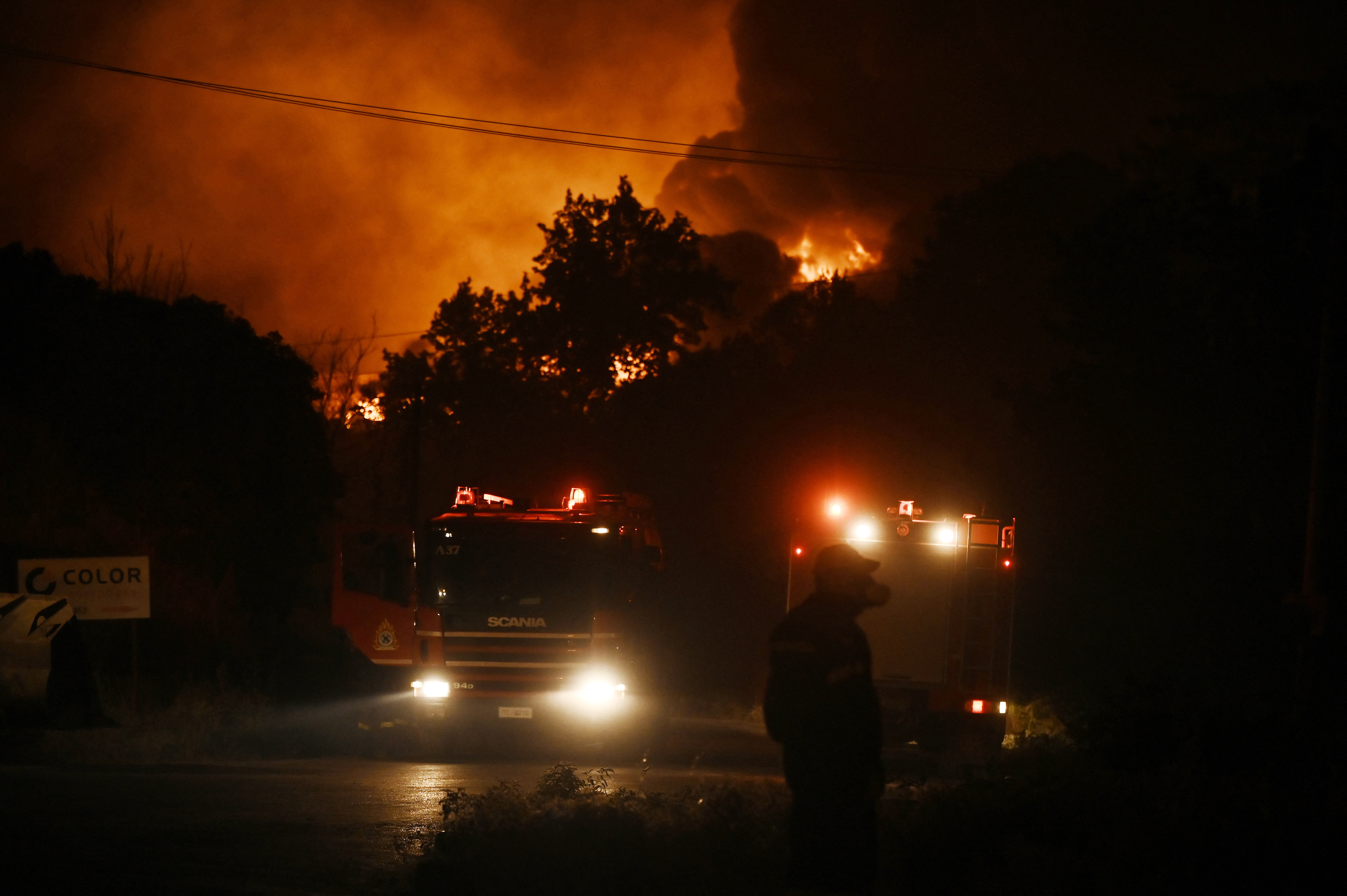 Flames light up the sky as a wildfire threatens nearby homes, while emergency personnel respond on the ground in Oreokastro, a suburb north of Thessaloniki, Greece, on July 5, 2026. (Photo by Sakis Mitrolidis / AFP)