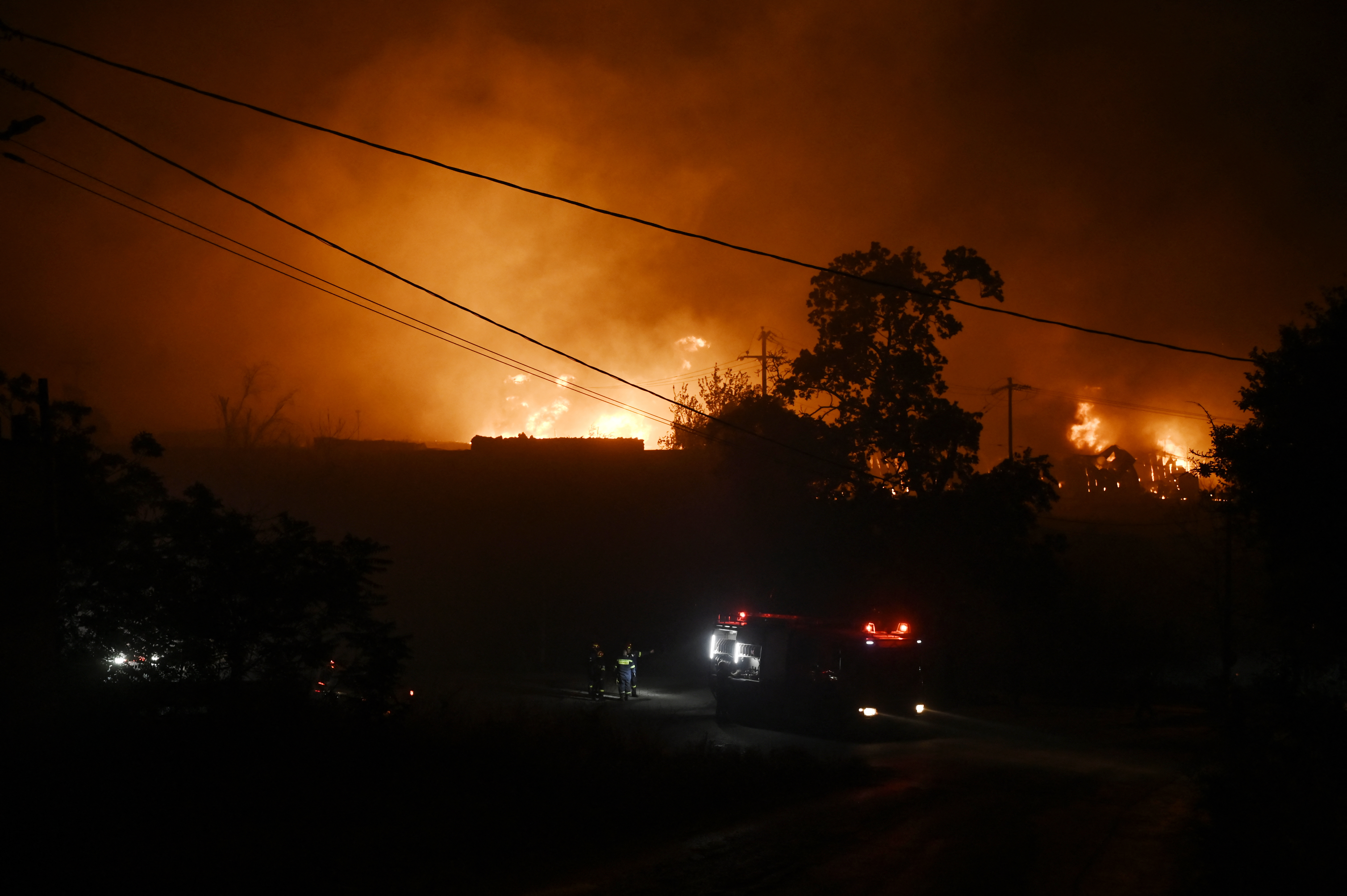 Flames light up the sky as a wildfire threatens nearby homes, while emergency personnel respond on the ground in Oreokastro, a suburb north of Thessaloniki, Greece, on July 5, 2026. (Photo by Sakis Mitrolidis / AFP)
