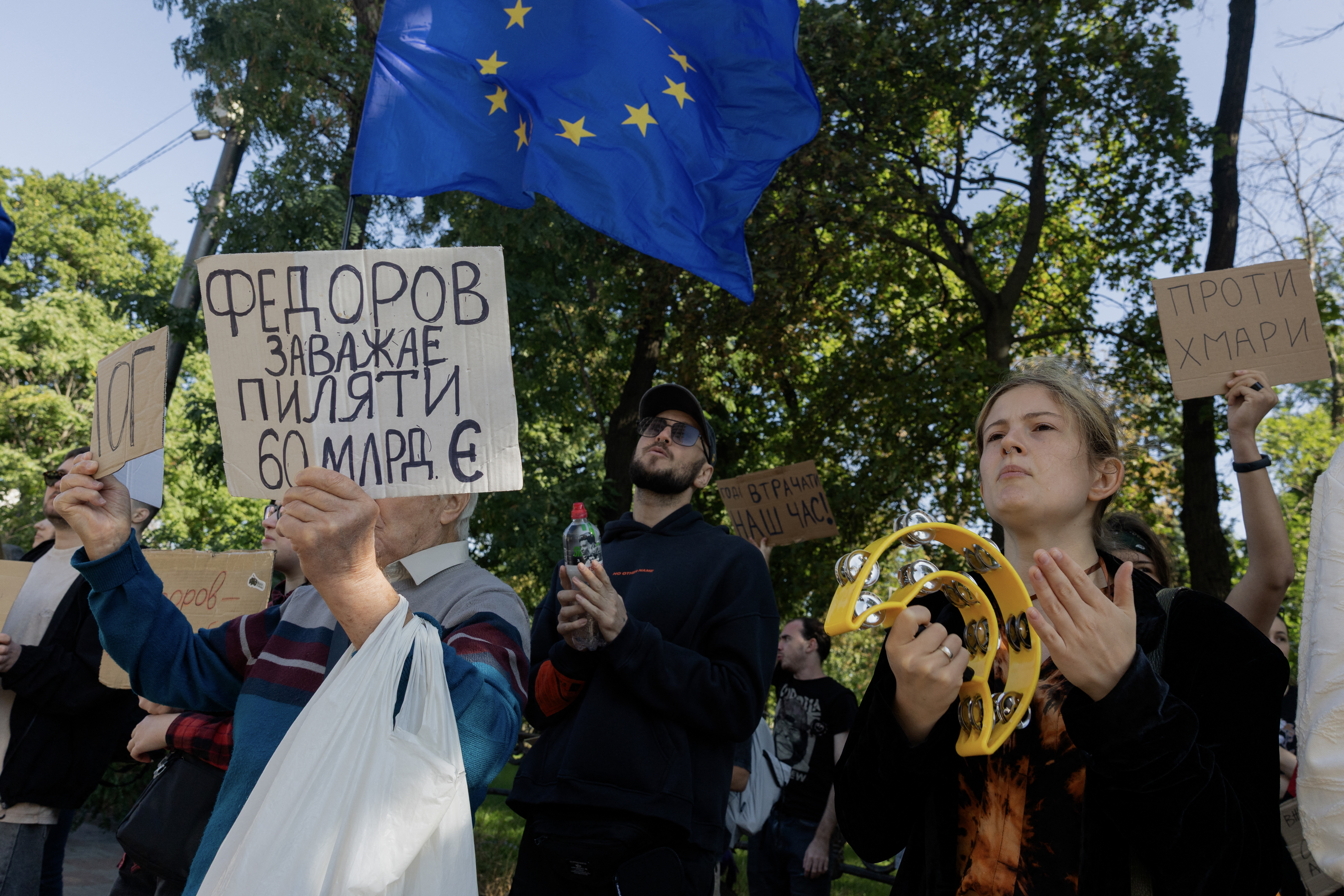 A protester holds a placard (L) reading "Fedorov is interferes the stealing of 60 million", in reference to Mykhailo Fedorov, a Ukrainian politician who served as Ukraine’s defense minister in 2026