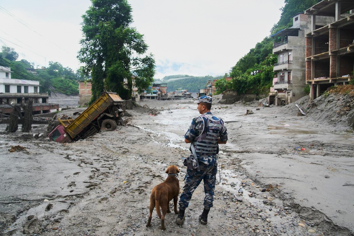 A policeman with a sniffer dog looks at the damage in the aftermath of flash floods. (AP Photo/Niranjan Shrestha)