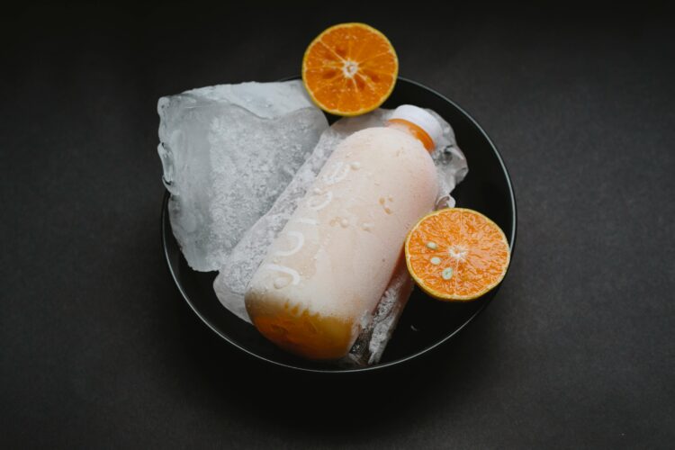zaleđena boca soka u zdjeli s velikim komadom leda, naranča prerezana napola