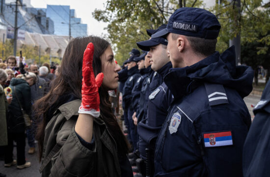 novi sad prosvjed, djevojka s podignutom rukom na kojoj je rukavica umočena u crvenu boju stoji ispred policajca