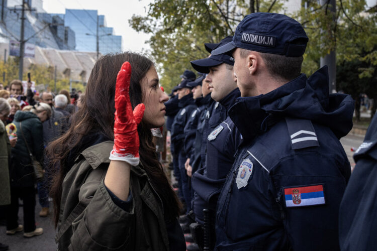 novi sad prosvjed, djevojka s podignutom rukom na kojoj je rukavica umočena u crvenu boju stoji ispred policajca