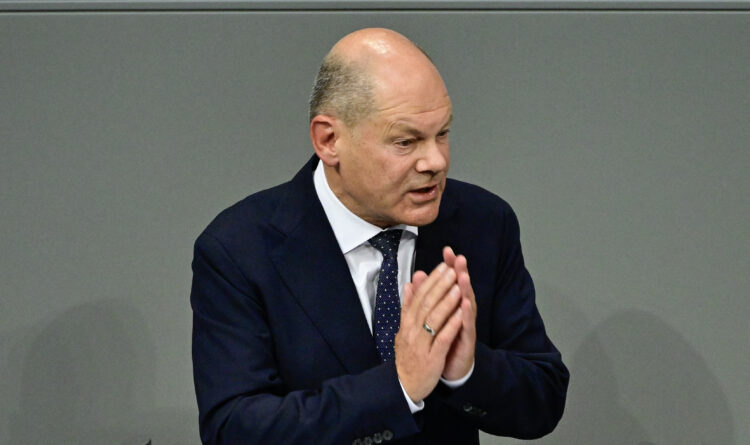 olaf scholz u odijelu i kravati sa spojenim dlanovima kao da moli krunicu